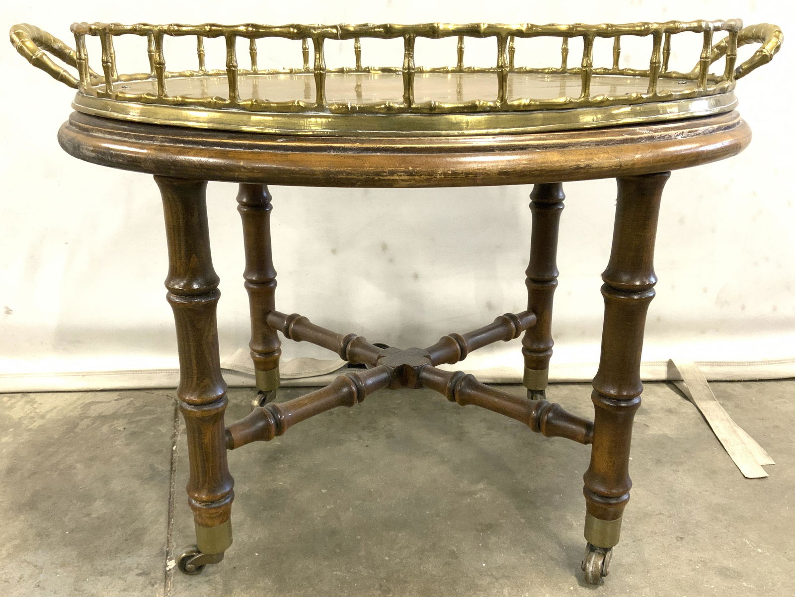 Vintage Oval Brass Tray On Stand W Casters: Tray table is vintage possibly antique. Tabletop is gold toned & brass with 2.5 inch tall gallery with handles on each side. Brass tray is attached to stand structure. Stand is wooden bamboo style, Ta