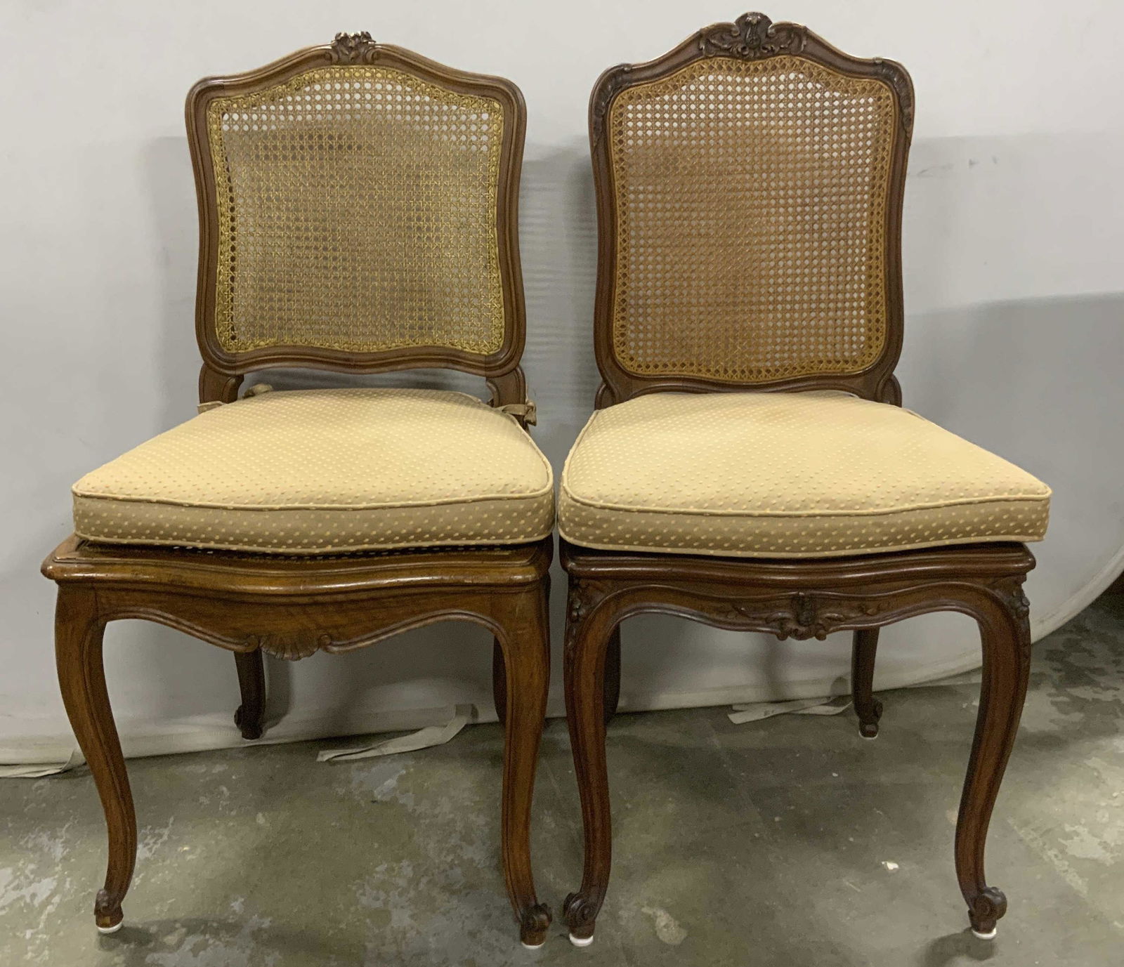 Pair Vintage Carved Wood Caned Side Chairs: Pair vintage, possibly antique, carved wooden side chairs. Backs and seats are crafted from woven cane. Legs are cabriole, apex of each chairs back is decorated with carved floral detailing. Each chai