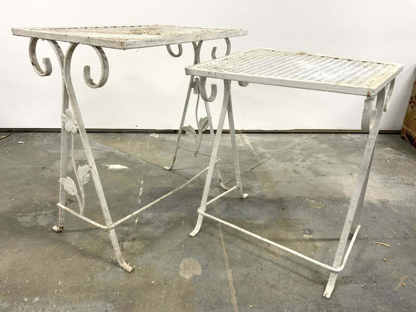 Pair Vintage Outdoor Metal Side Tables: Side tables are vintage possibly antique. Each are white toned and metal. One has floral & leaf structures in between legs. Largest table measures approx 20 inches tall 18.5 inches long 13 inches deep