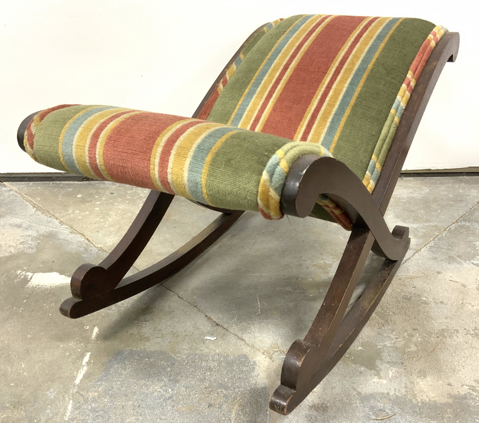 Antique Upholstered Children’s Rocking Chair: Rocking chair is vintage possibly antique. Chair has carved wooden frame. Piece is upholstered with multi toned striped fabric with double welting at edges. Piece measures approx 23 inches long 15 inc