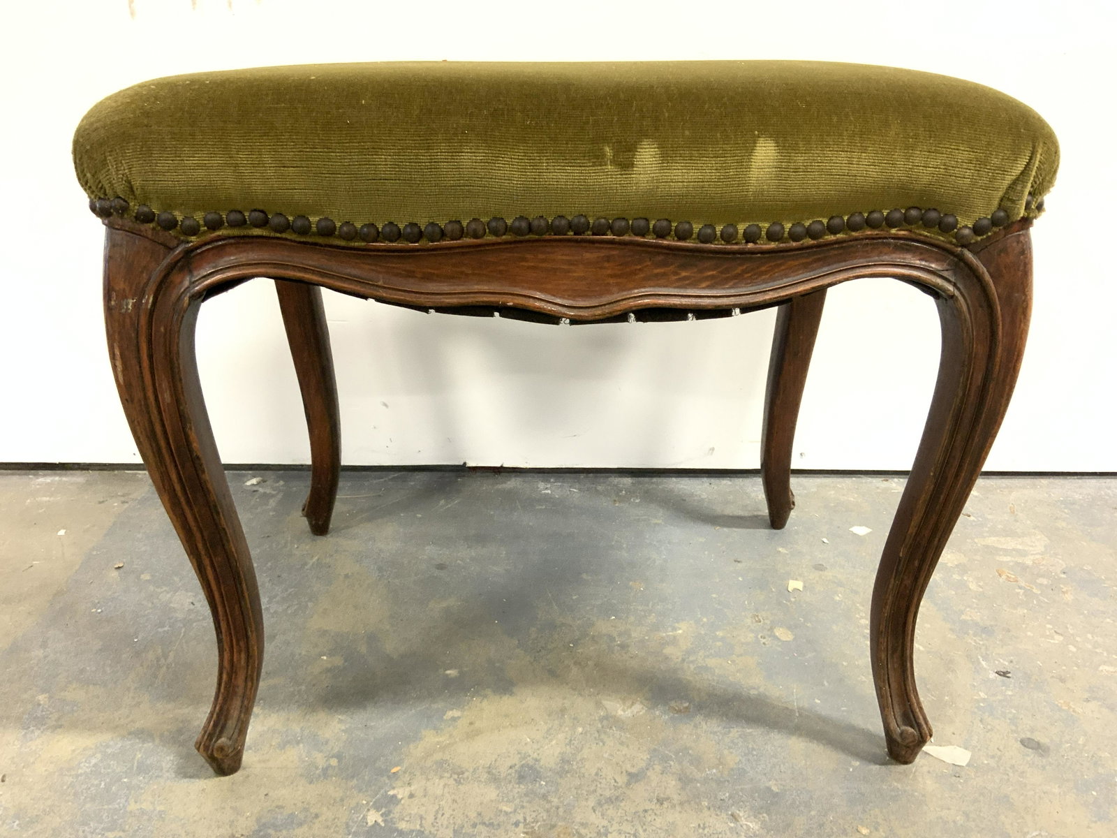 Vintage Upholstered Wooden Bench W Nailhead Detail: Bench is vintage possibly antique. Piece has dark olive toned upholstery with nailhead detail at edges. Piece has brown toned carved wooden legs. Upholstery appears to possibly be crushed velvet. Piec