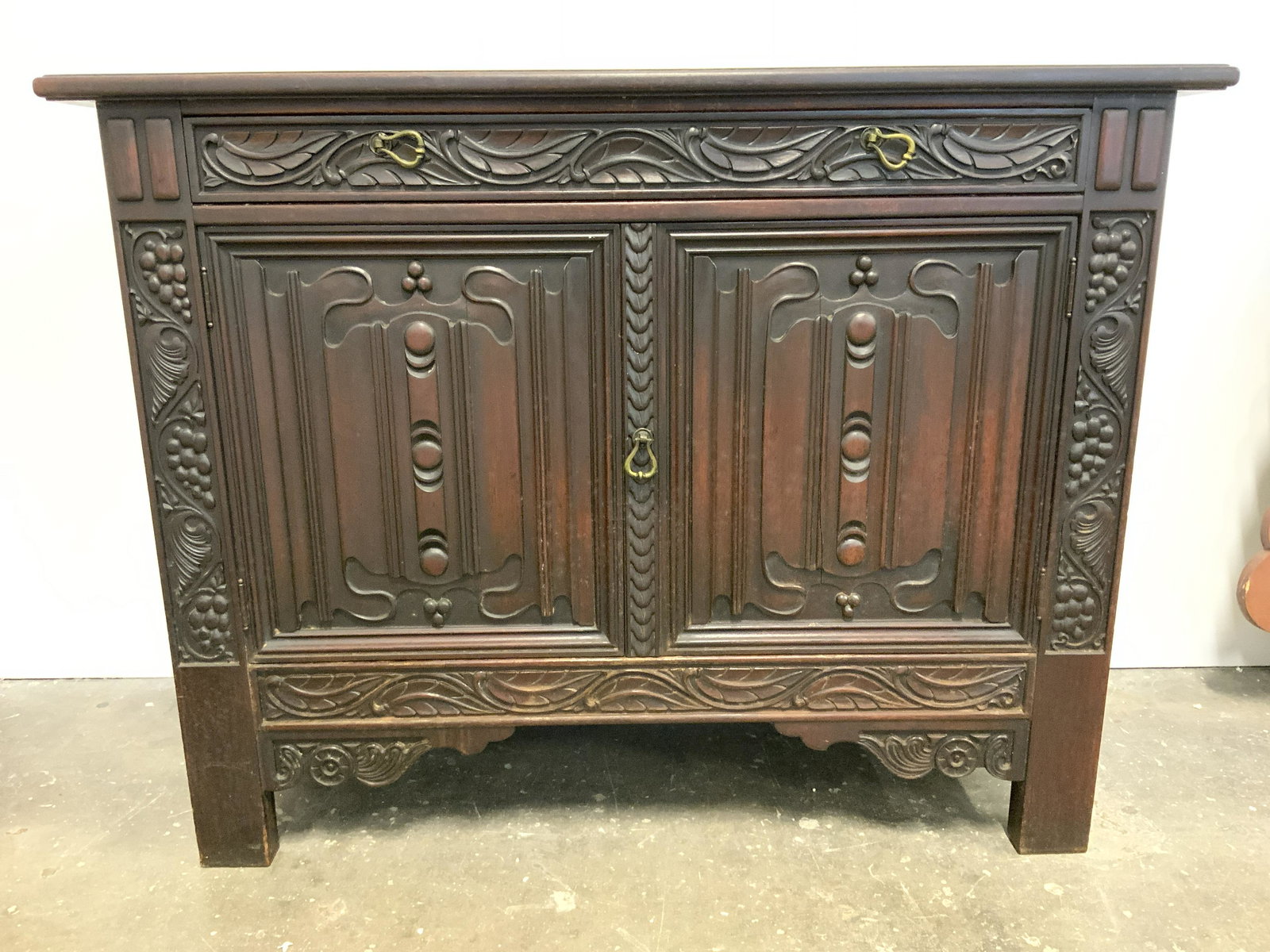 Vintage Carved Wooden Silverware Drawer W Cabinets: Piece is vintage possibly antique. Cabinet has intricately carved geometric, grape & vine detail. Piece has 2 cabinet doors with 1 shelf inside. Piece appears to be hand crafted. Drawer has 2 gold ton