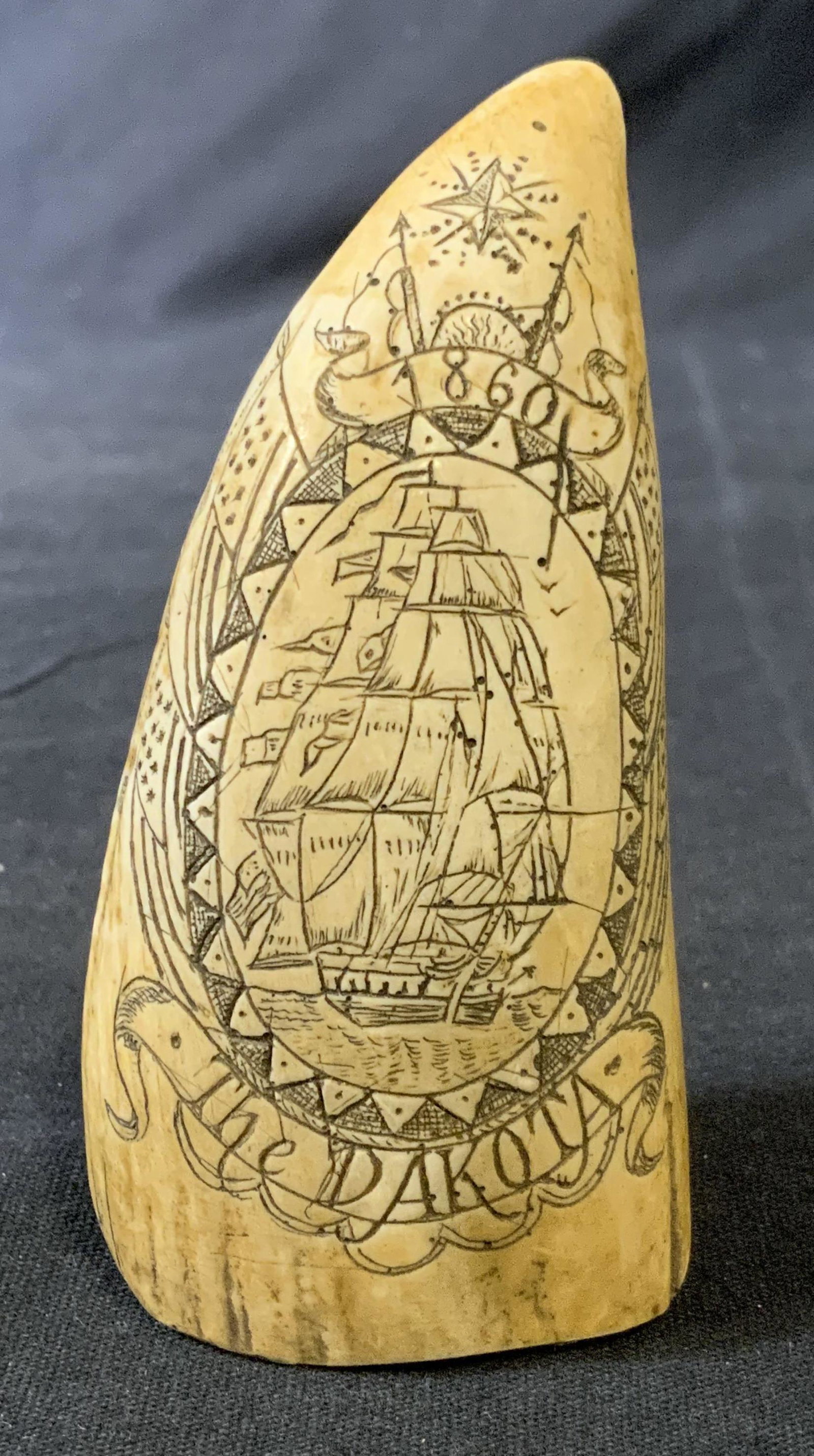 THE DAKOTA Faux Scrimshaw Etched Resin Tooth: Faux scrimshaw tooth, appears to be sculpted from resin. Etching depicts a whaling ship, the banner beneath the ship reads as THE DAKOTA, 1860, the back of the tooth reads as NANTUCKET. Measures appro