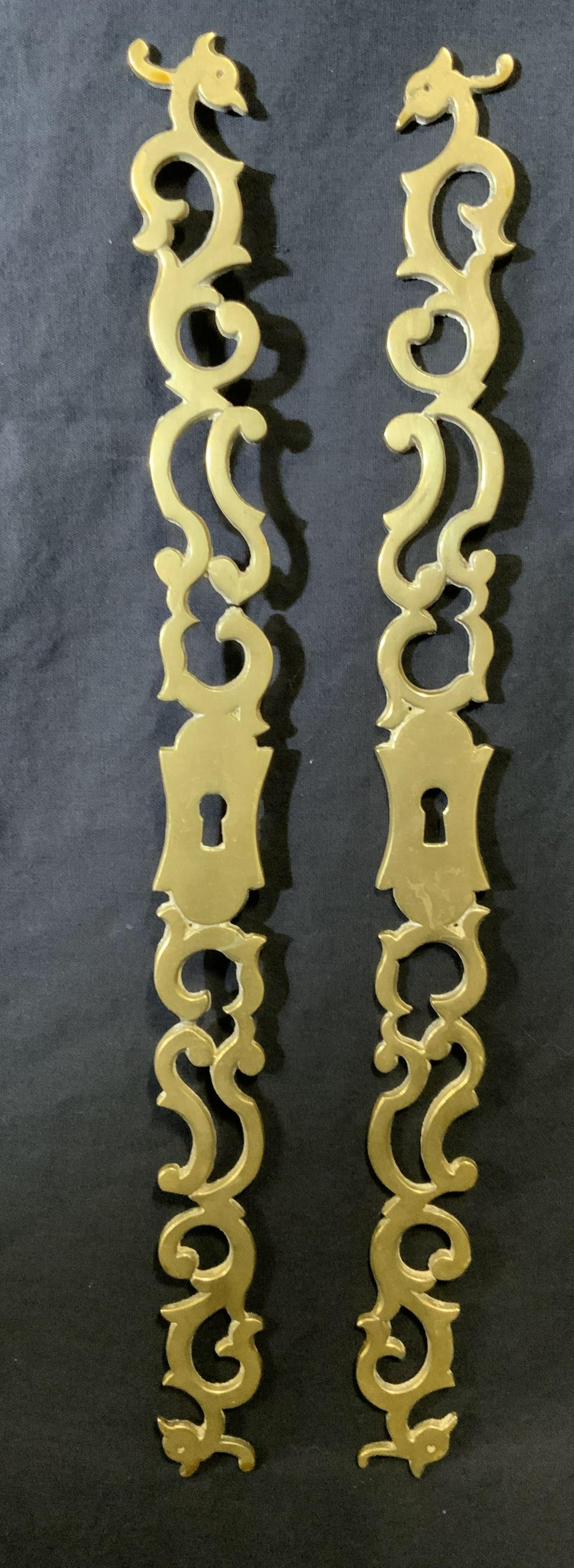 Pair Pierced Brass Escutcheons: Pair of brass escutcheons. Each is pierced, the ends resemble the heads of birds. The keyhole is found in the center. Each measures approx 15.25 inches Long, and 1.25 inches W. Property of Janine Metz