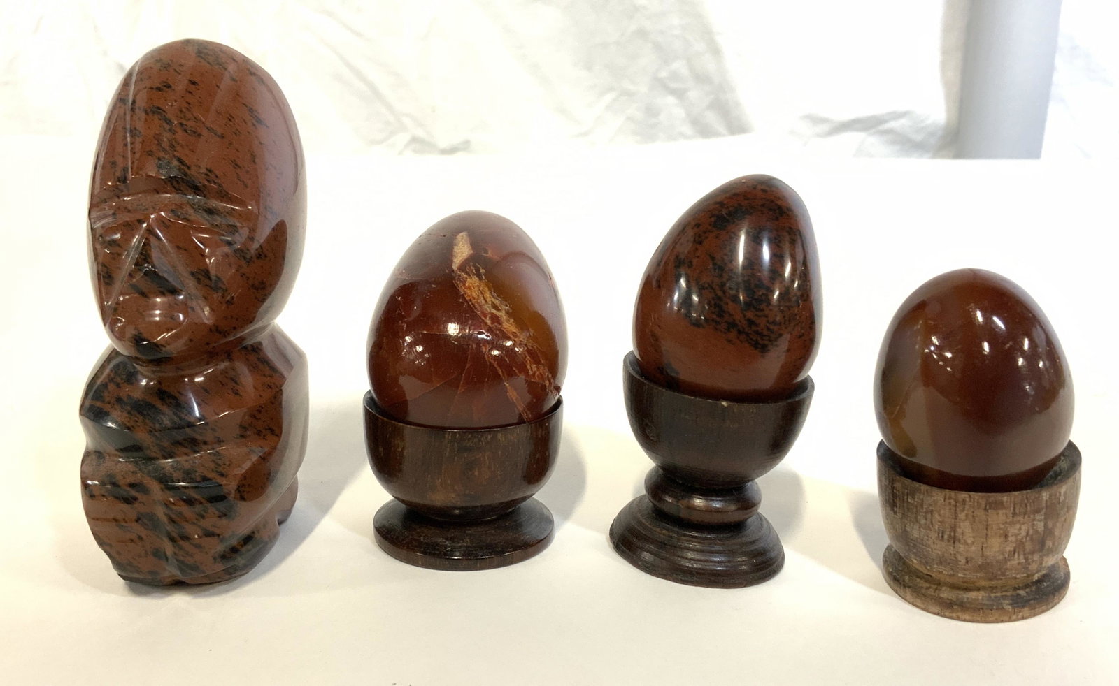 Lot 4 Polished Stone Accessories: Lot of 4 polished stone accessories. Carved stone accessories, includes 3 polished stone eggs, with stands, and a carved stone totemic figure. All are rust toned. Largest measures approx 4 inches H, a