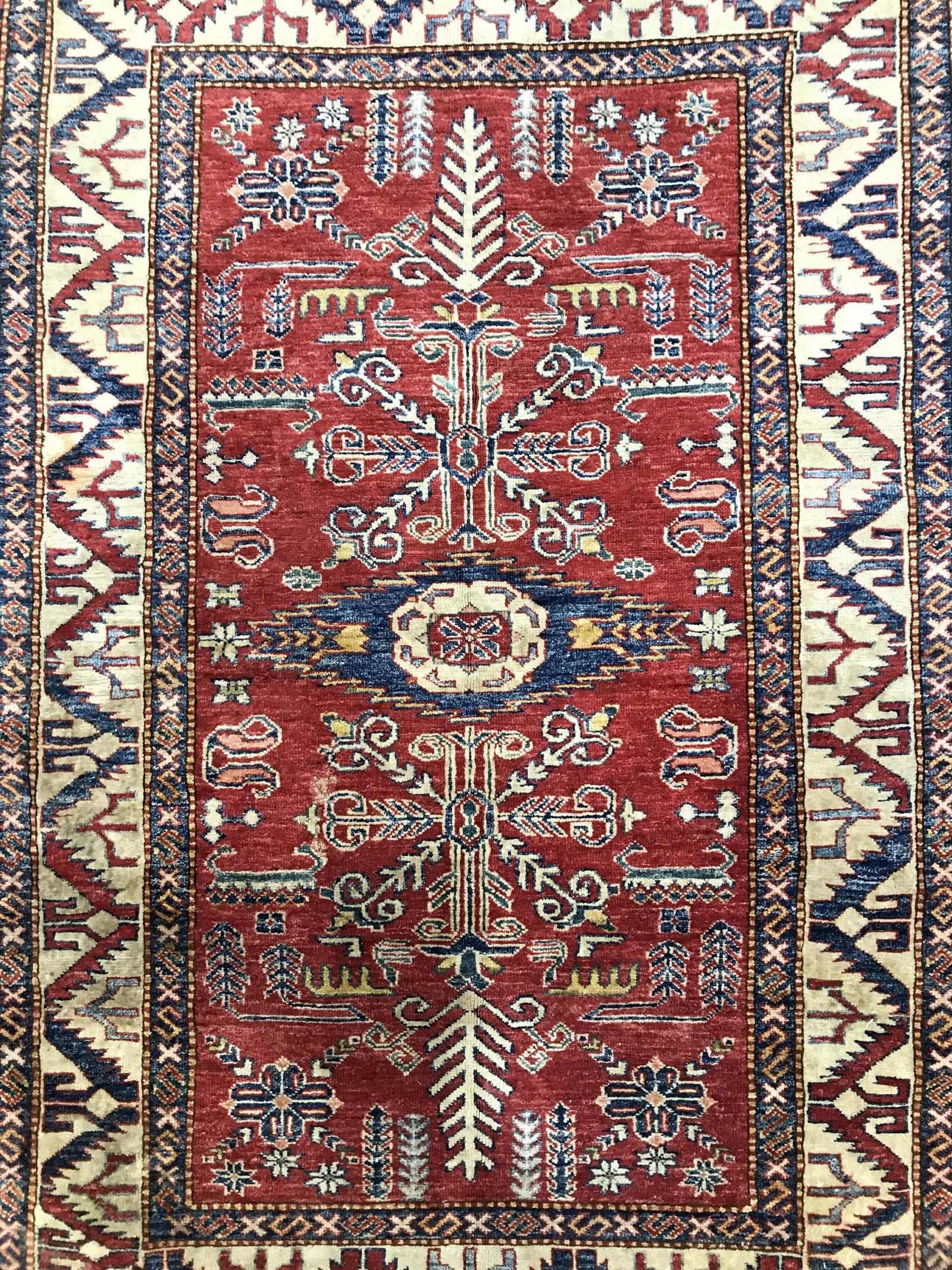 Vintage Handmade Fringed Wool Rug: Rug is vintage possibly antique. Piece appears to be Turkish. Contains sand, re and blue toned geometric detail. Edges of rug are fringed. Piece measures approximately 74 inches long 48 inches wide. R