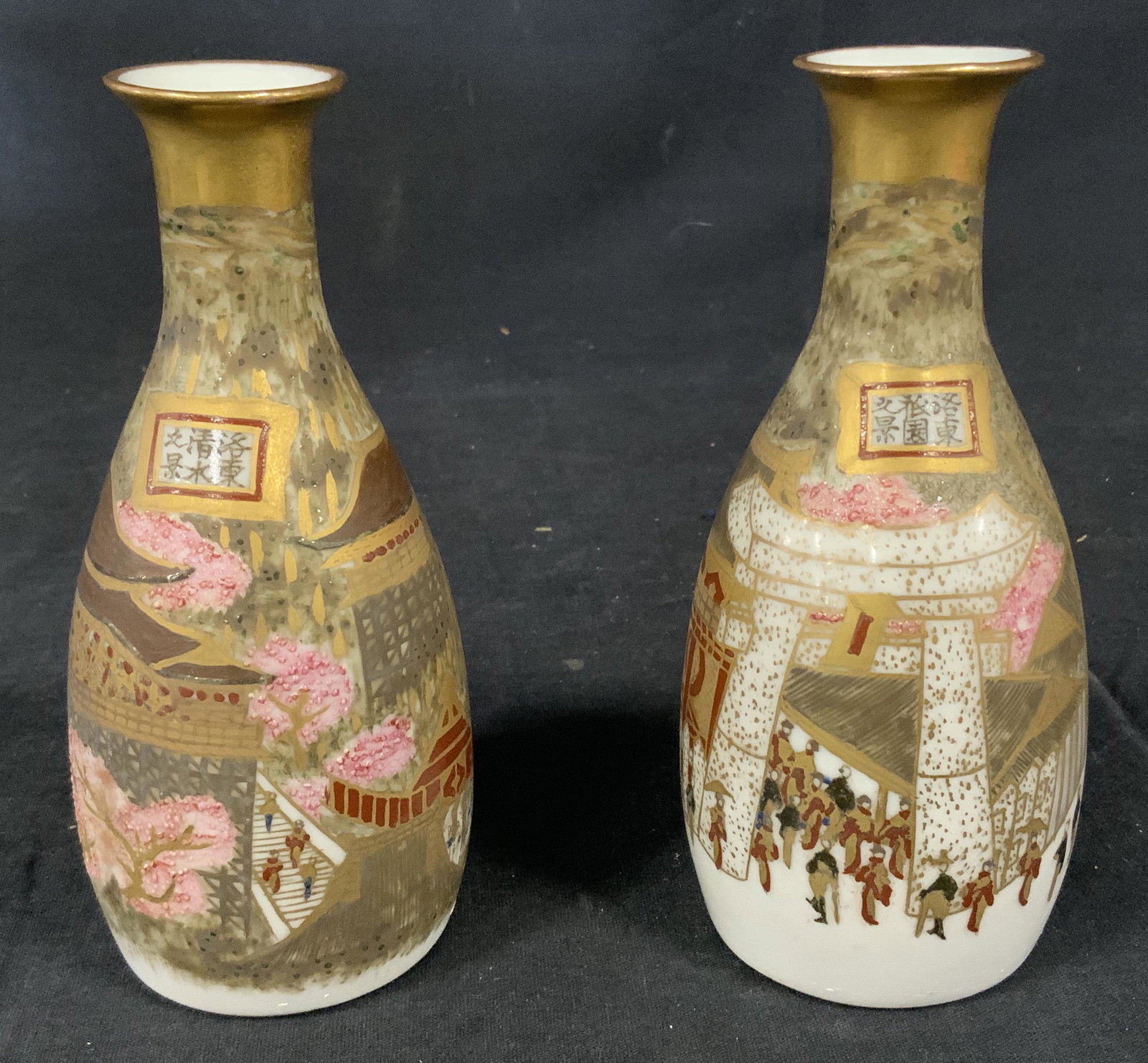 Pair Hand Painted Ceramic Sake Flasks: Pair of hand painted ceramic sake flasks, possibly vintage. Each decorated with an illustration depicting a townscape, groups of people, and blossoming cherry blossom trees. Asian characters, framed i