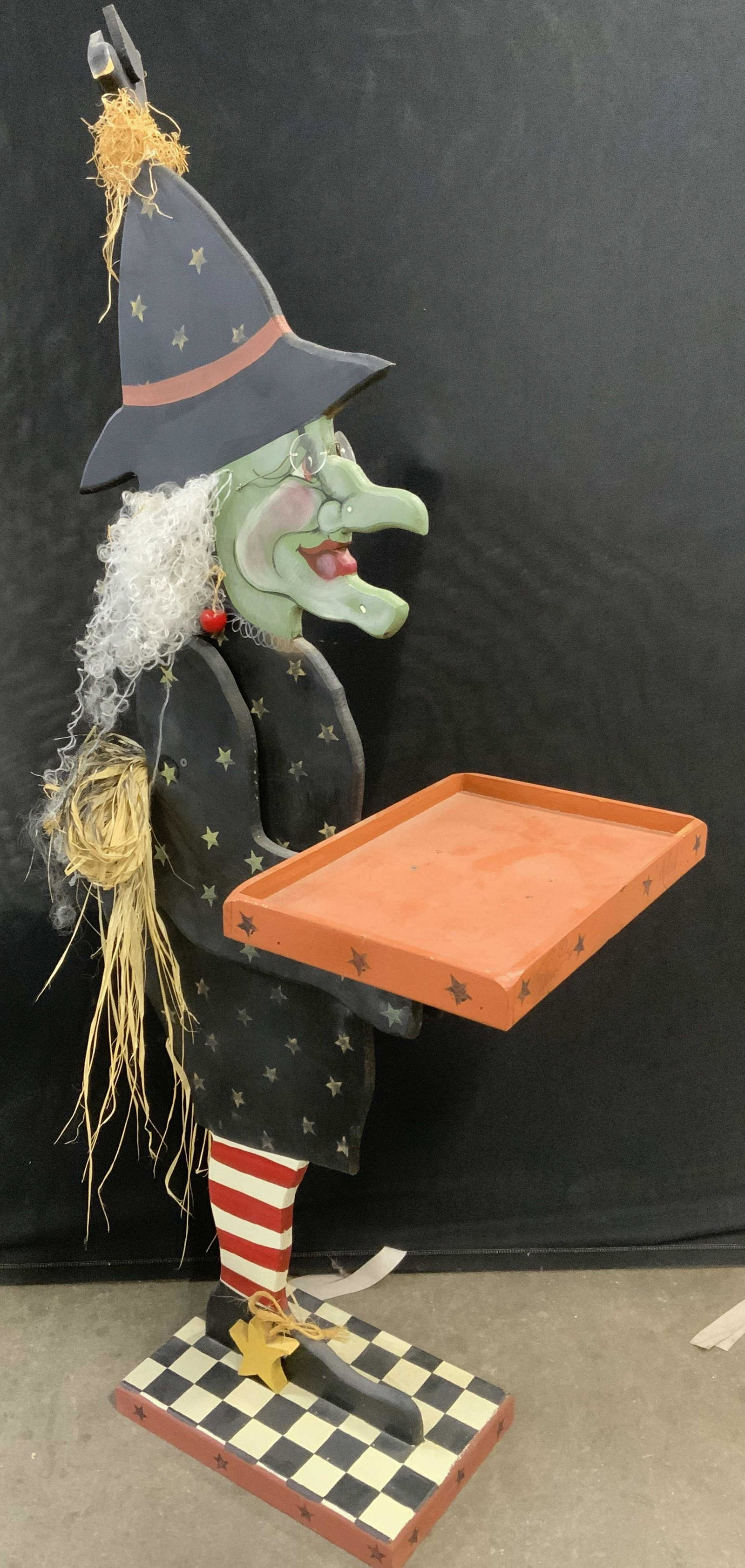Floor Size Folk Art Wooden Witch Statue 52.5 in H: Floor size kitchen witch. Crafted from wood, depicts a witch holding a tray. A bird is nesting on her hat, and her belt is crafted from straw. Carved star shape detailing decorates the piece. The witc