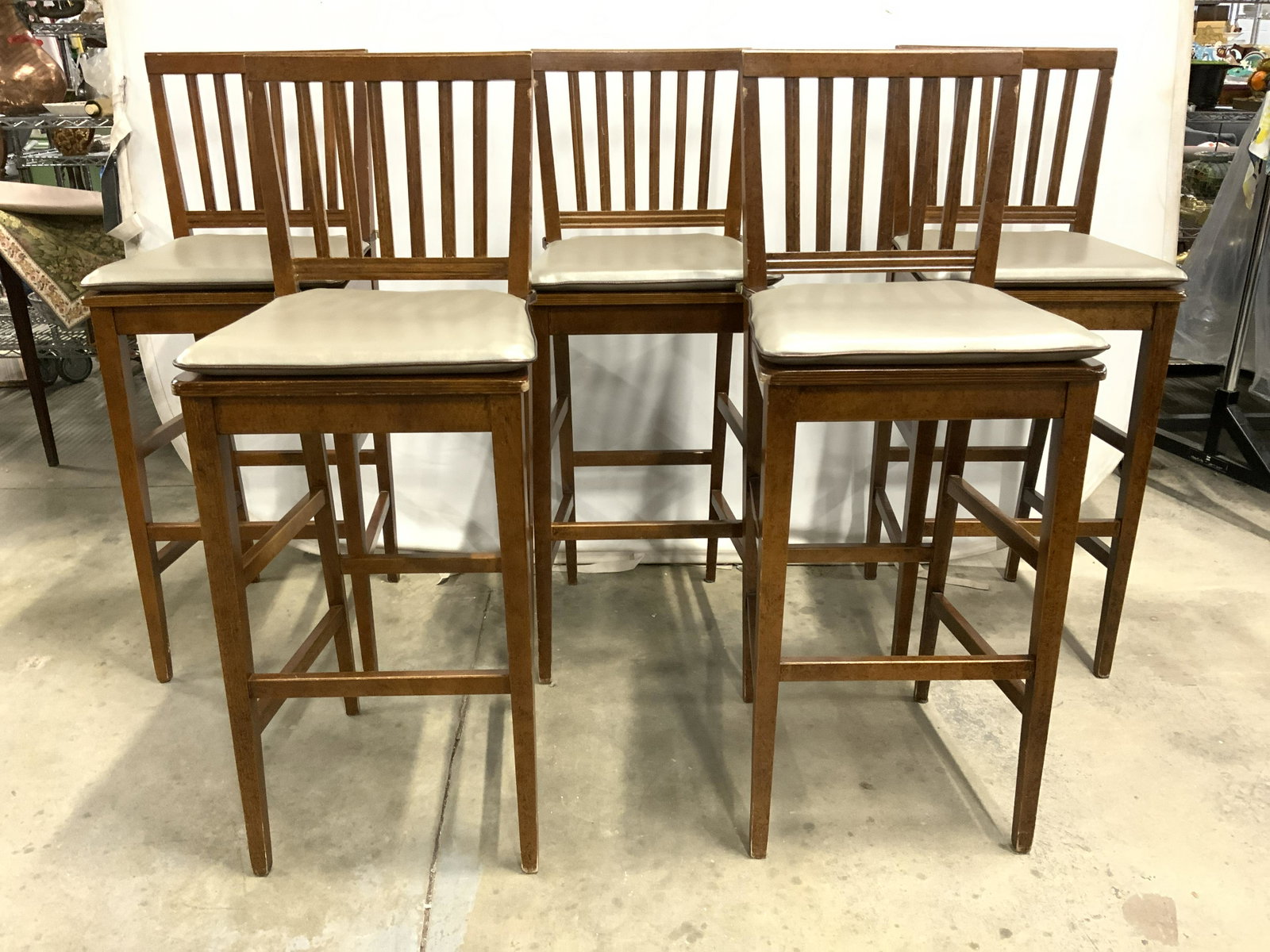 Set 5 BUYING & DESIGN Italian Wooden Stools: Each stool has tag on underside which reads BUYING & DESIGN MADE IN ITALY. Each stool is brown toned and wooden with angular spindle back rests. Each seat includes slate toned cushions, possibly leath
