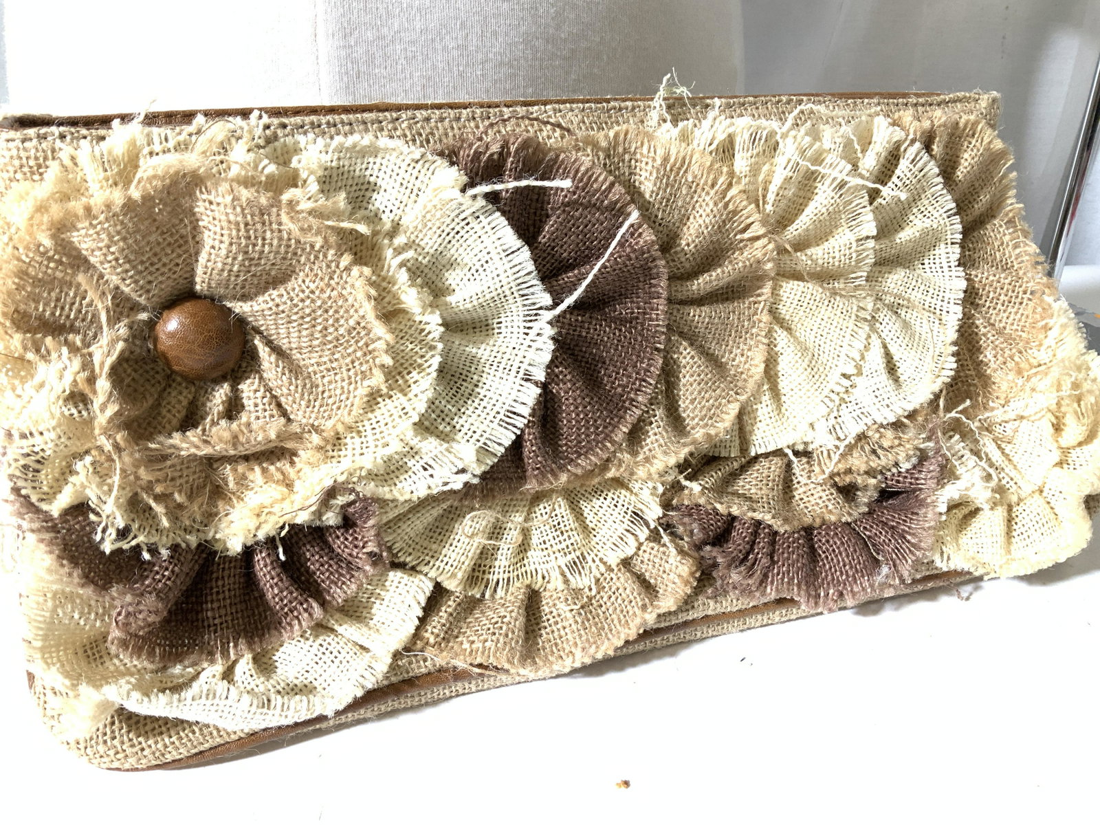 Ladies Flower Burlap Large Tuck Under Clutch: Woven burlap, natural tones, plisse flowers on front, zippered closure, clean satin style fabric interior. Zippered interior pocket, couple pouches. Measures 14.5 in. L, 8 in. Ht. Tucks under arm. Bur