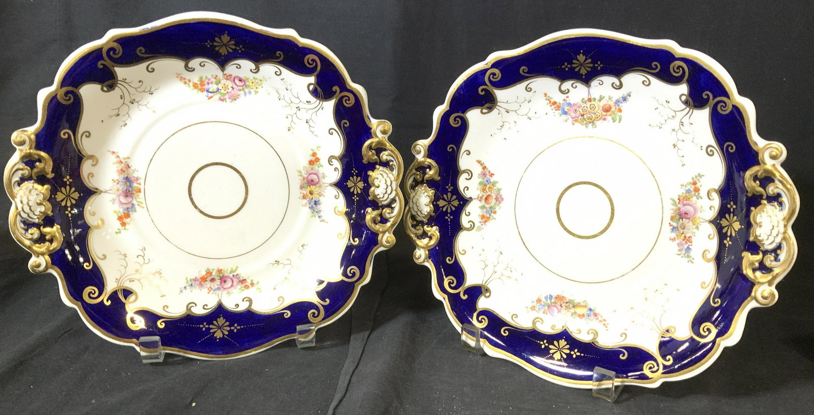 Pair Hand Painted European Porcelain Plates: Rich Gilt scroll work on the embossed handles and outlining the deep cobalt blue plate border. Hand painted, bunches of flowers, stark white porcelain. One plate marked With letter A, other plate mark