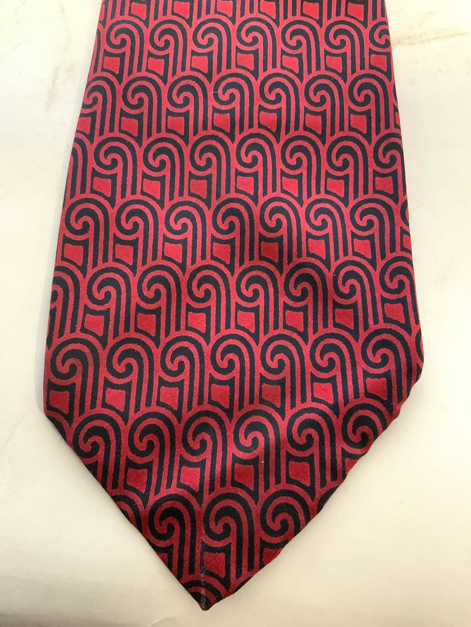 GIVENCHY Men’s Patterned Silk Necktie: Tag reads GIVENCHY ALL SILK PARIS NEW YORK. Necktie is silk. Piece is red with navy toned geometric detailed pattern. Inner area has “GIVENCHY” in gold toned lettering in a diagonal pattern. Piece