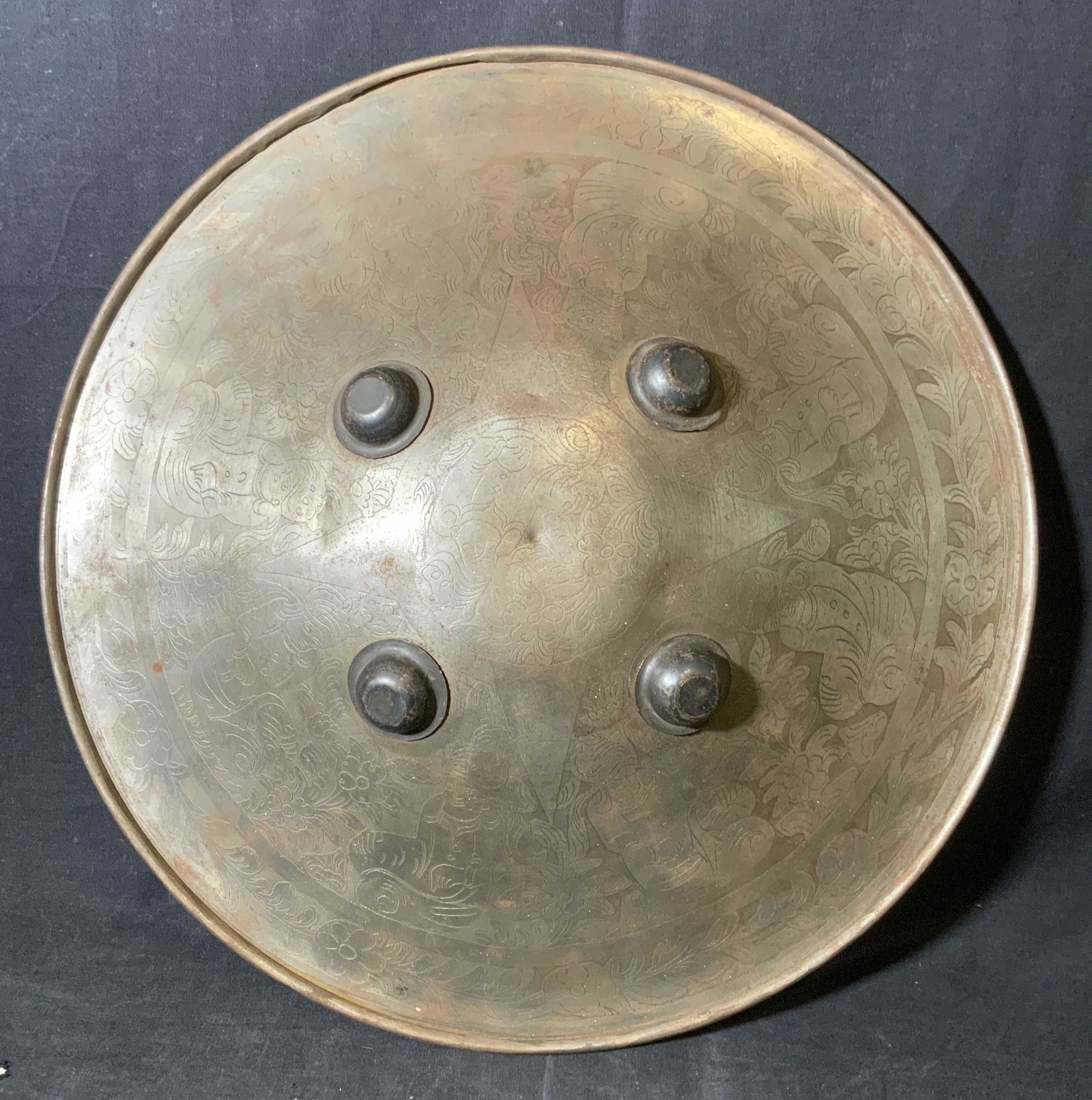 Vintage Persian Style Metal Shield: Decorative metal shield, Persian styled. Decorated with etchings of robed men sitting amongst flowers. Measures approx 19 inches in diameter. Robe affixed to back allows for hanging of shield. Wear is