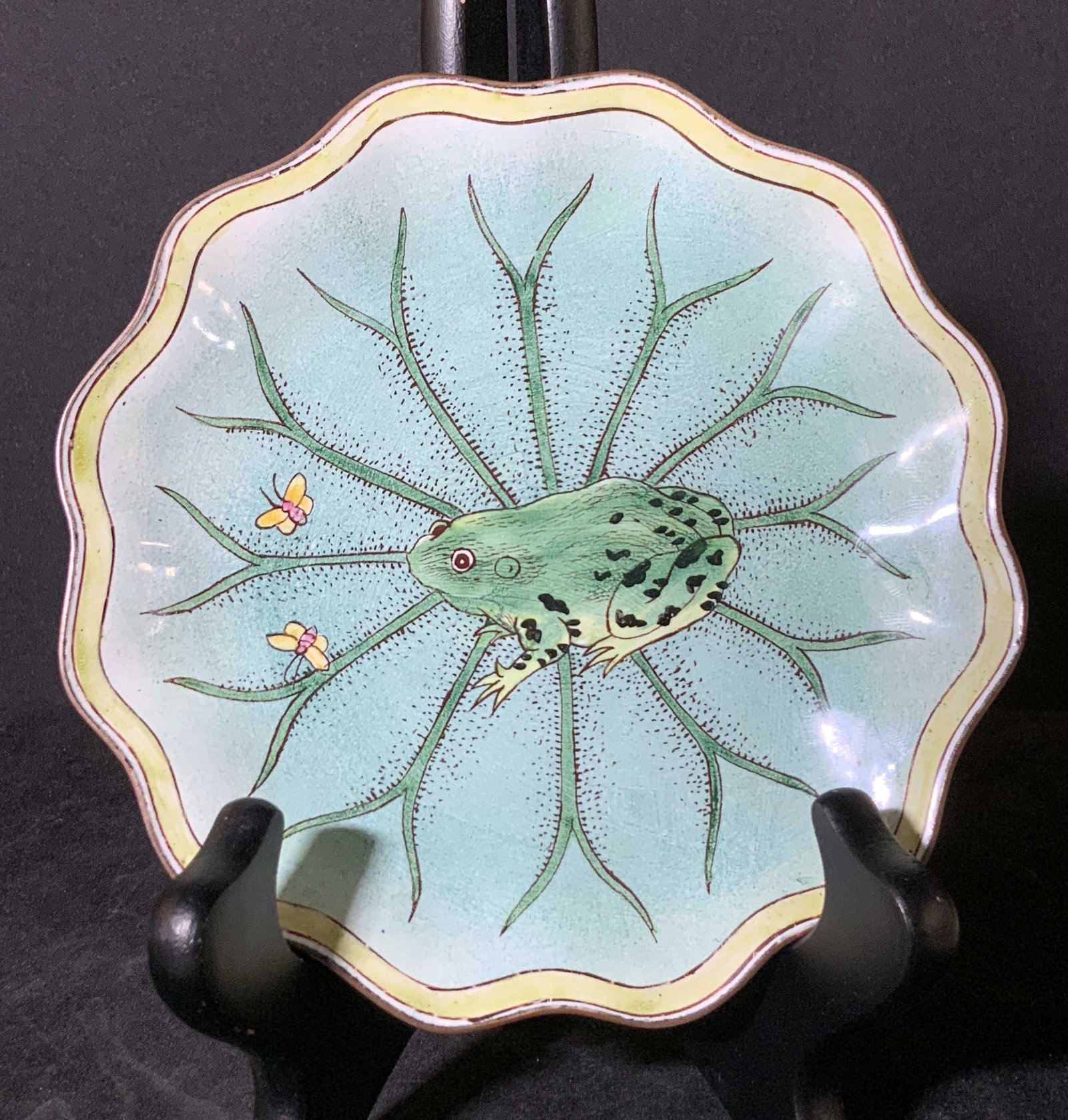 KELVIN CHEN Signed & Numbered Enamel Frog Dish: A handmade, artisan enameled metal dish depicting a frog and two butterflies. The rim of the dish is scalloped, mimicking a frog’s lily pad. The frog is depicting sitting and staring at the two butt