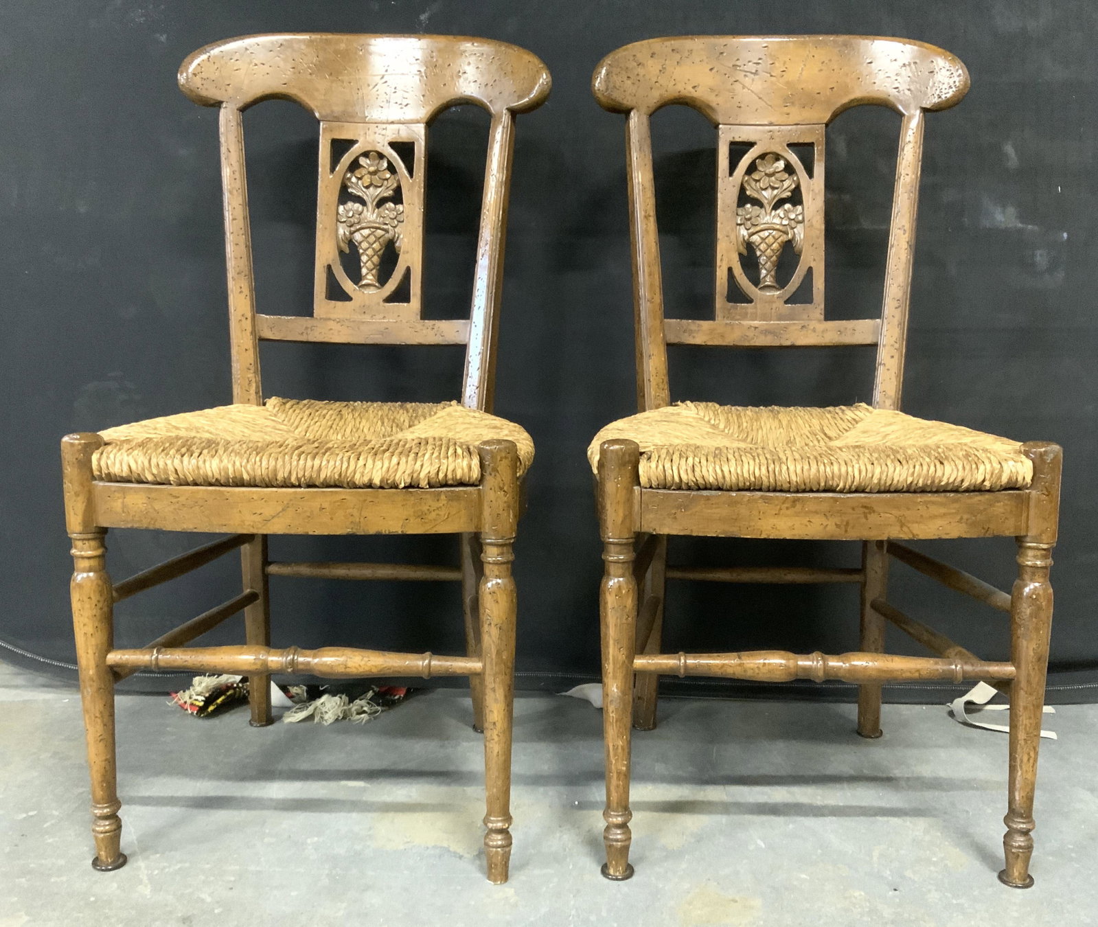 Pair Rush Seat Wooden Country French Chairs: Lot includes 2 chairs. Each are vintage possibly antique. Chairs are country French and includes intricately carved wooden detail to backrest depicting flowers & leaves in a vase. Both chairs have rus