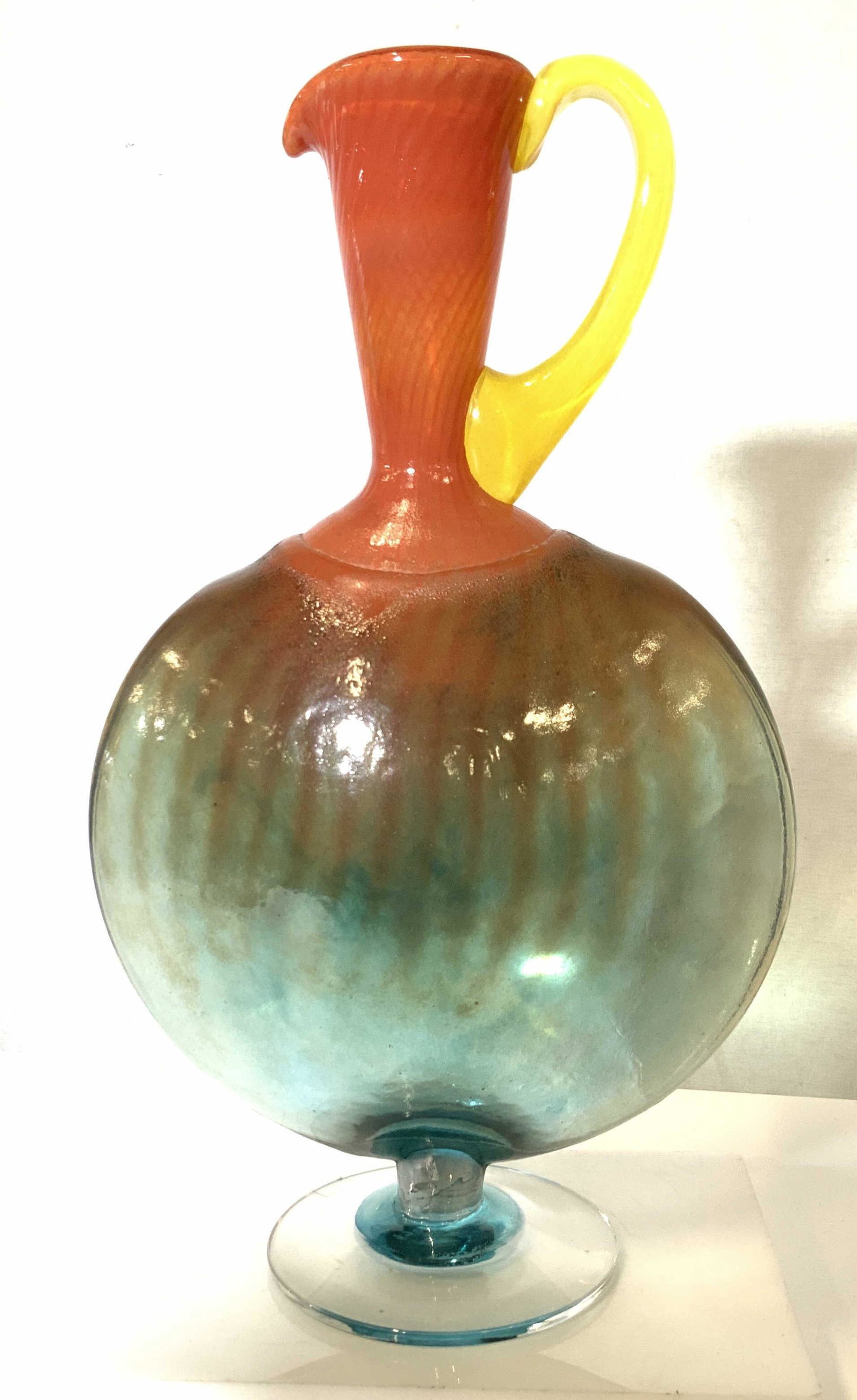 KOSTA BODA Ewer Art Glass Pitcher, signed ENGMAN: THICK WALLED art glass ewer with yellow handle, orange trimmed spout that bleeds into the light blue body. The piece measures about 13.5 in. high, 8.5 in. W. Designed by well known artist KJELL ENGMAN