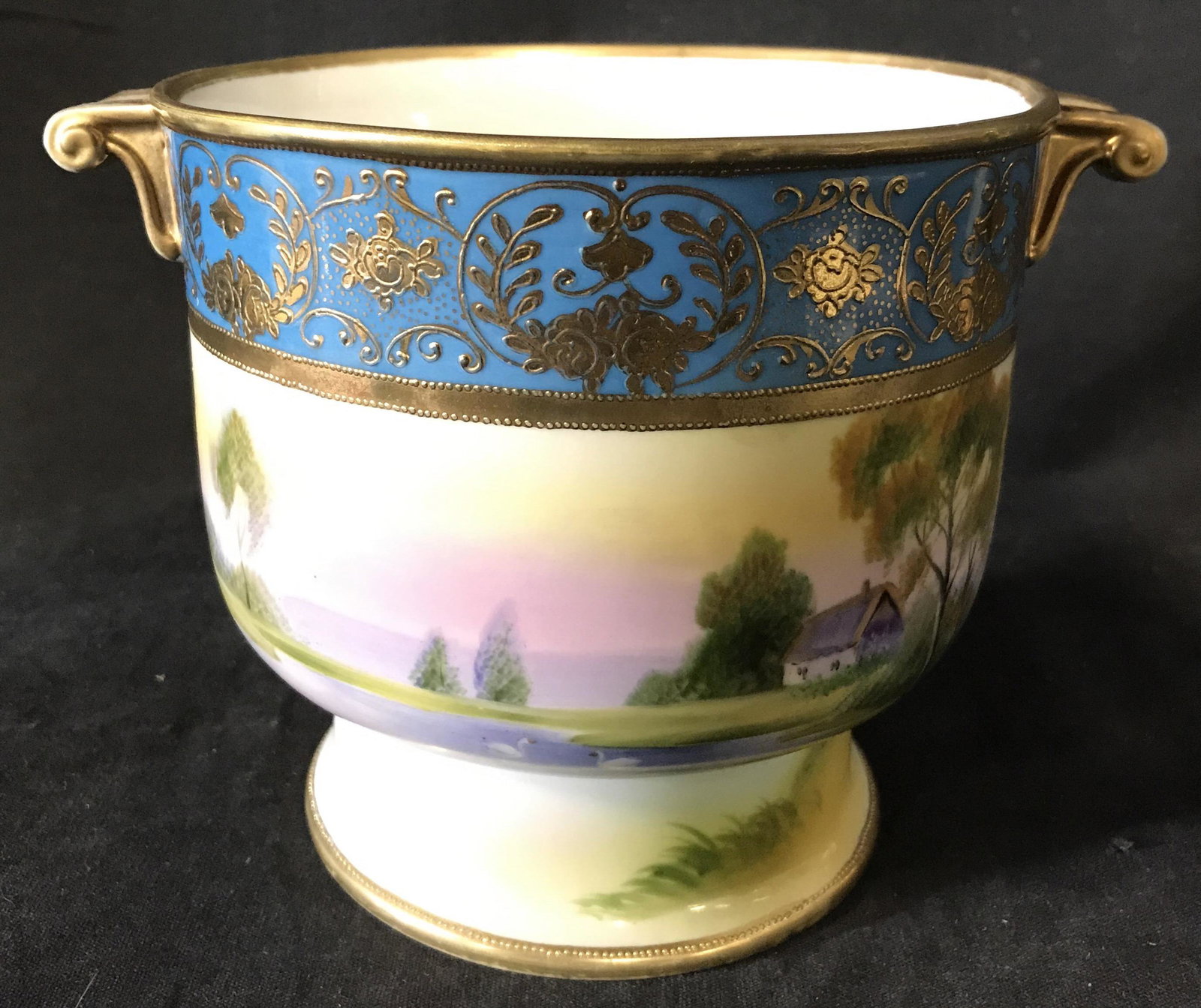 Antique Hand Painted Porcelain Vessel, JAPAN: Hand painted porcelain vessel. Underside marked as HAND PAINTED NIPPON. Depicts a lake front property, handles are gilded, a gilt paint and turquoise pattern decorates the rim. Measures approx 5.25 in