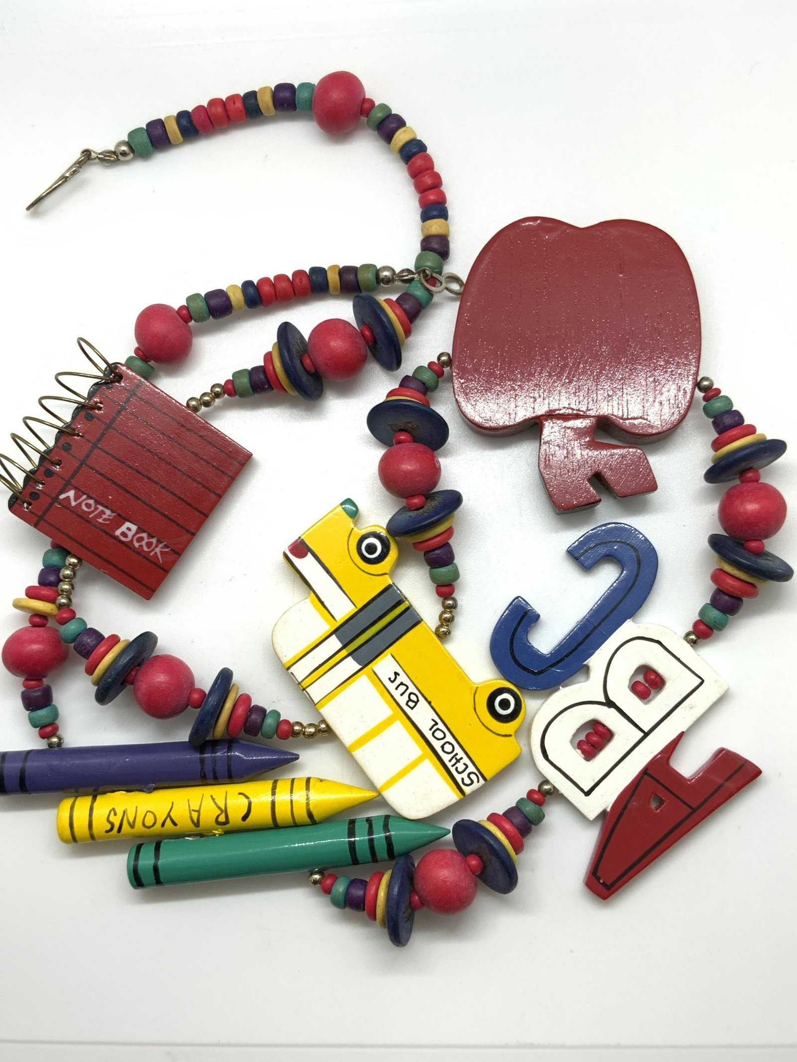 Vintage Chunky Wood School Teacher Motif Necklace: A vintage necklace comprised of painted wooden beads and charms. charms revolve around school. There is a bus, apple, crayon, notebook, and ABC letter charm. All pieces of this necklace are bright & v