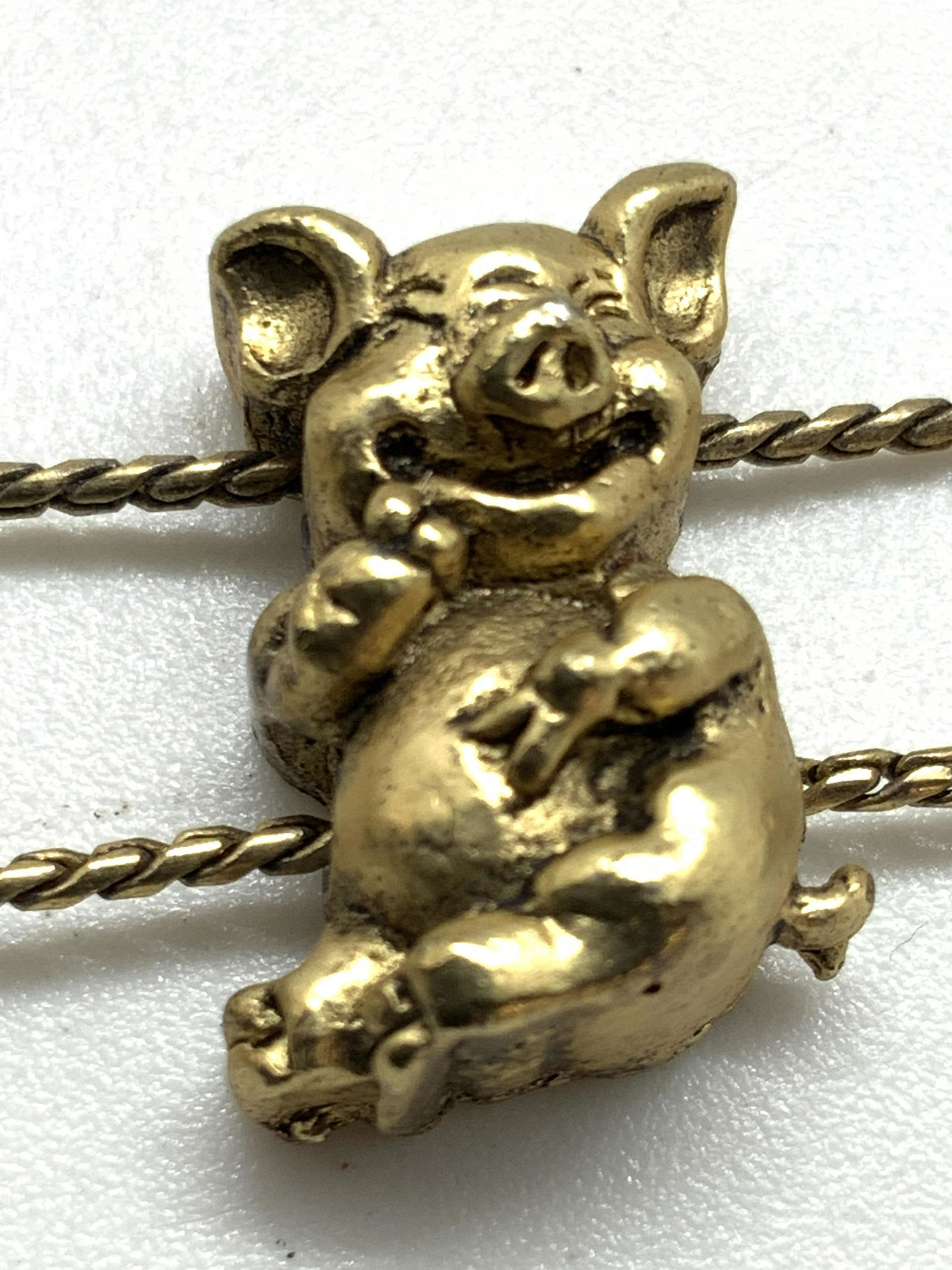 LAUGHING PIGS Etched Bracelet, Jewelry: A gold tone metal bracelet adorned with etched metal pig charms. The pigs are all connected via the double string that has strung the bracelet together. Etched and embossed metalwork details in each p