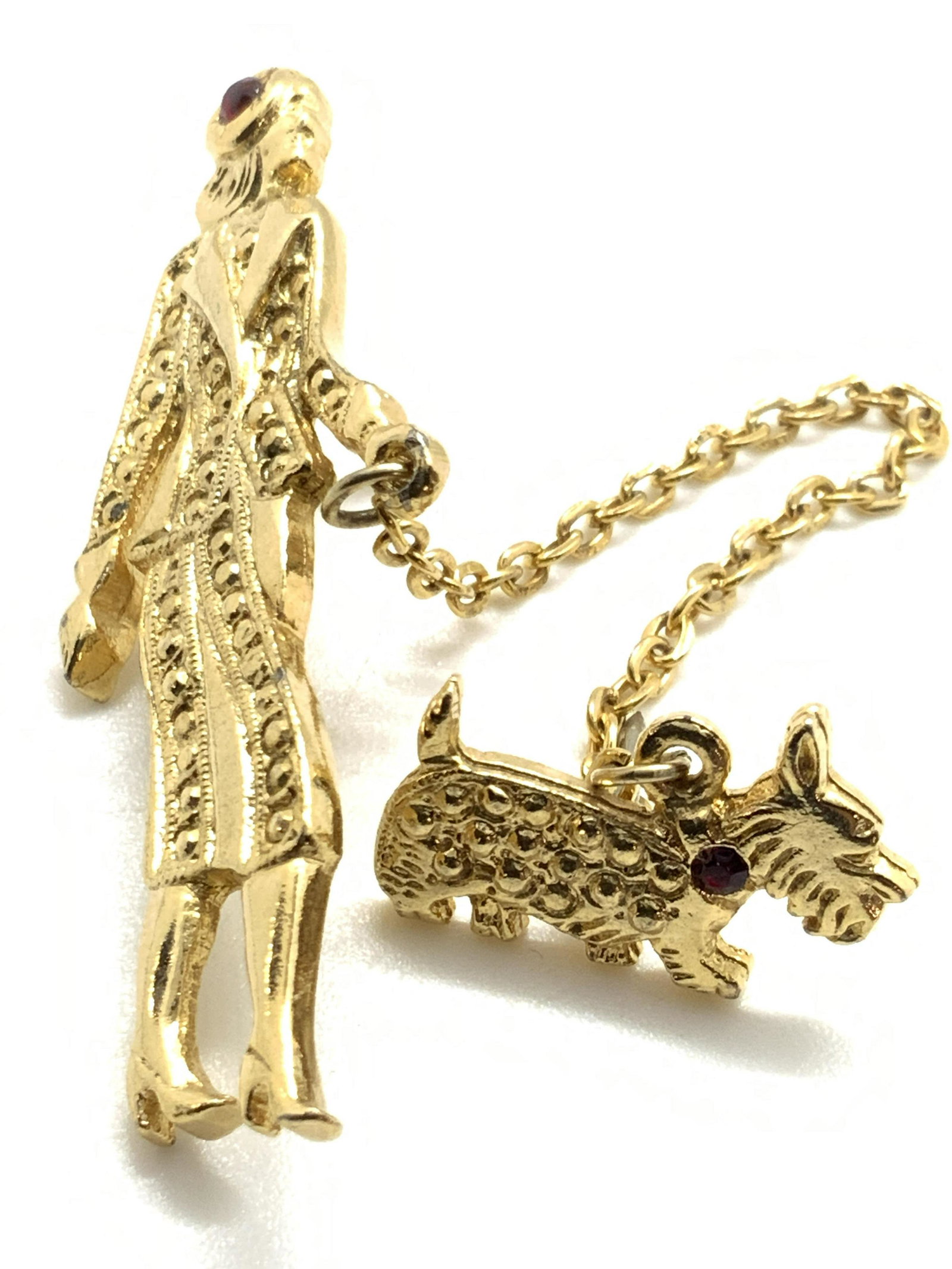 Woman Walking Dog Sweater Pin, Jewelry: A textured gold tone metal sweater pin featuring a woman in business attire walking a Scottish Terrier dog. Both feature deep red rhinestones. The pieces are connected by a gold tone chain. Undersides