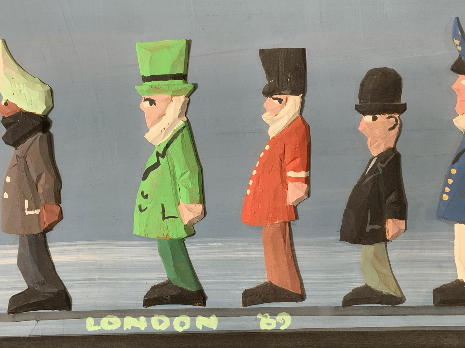 Vintage Framed British Wood Folk Art: Carved Wood Figural men standing in a line, pasted on board, in black wood frame, signed LINDON ‘89. Big Ben clock tower in background. 16.25 x 6.5 in. Framed at Walker Frame Shop in Westport, Ct, p