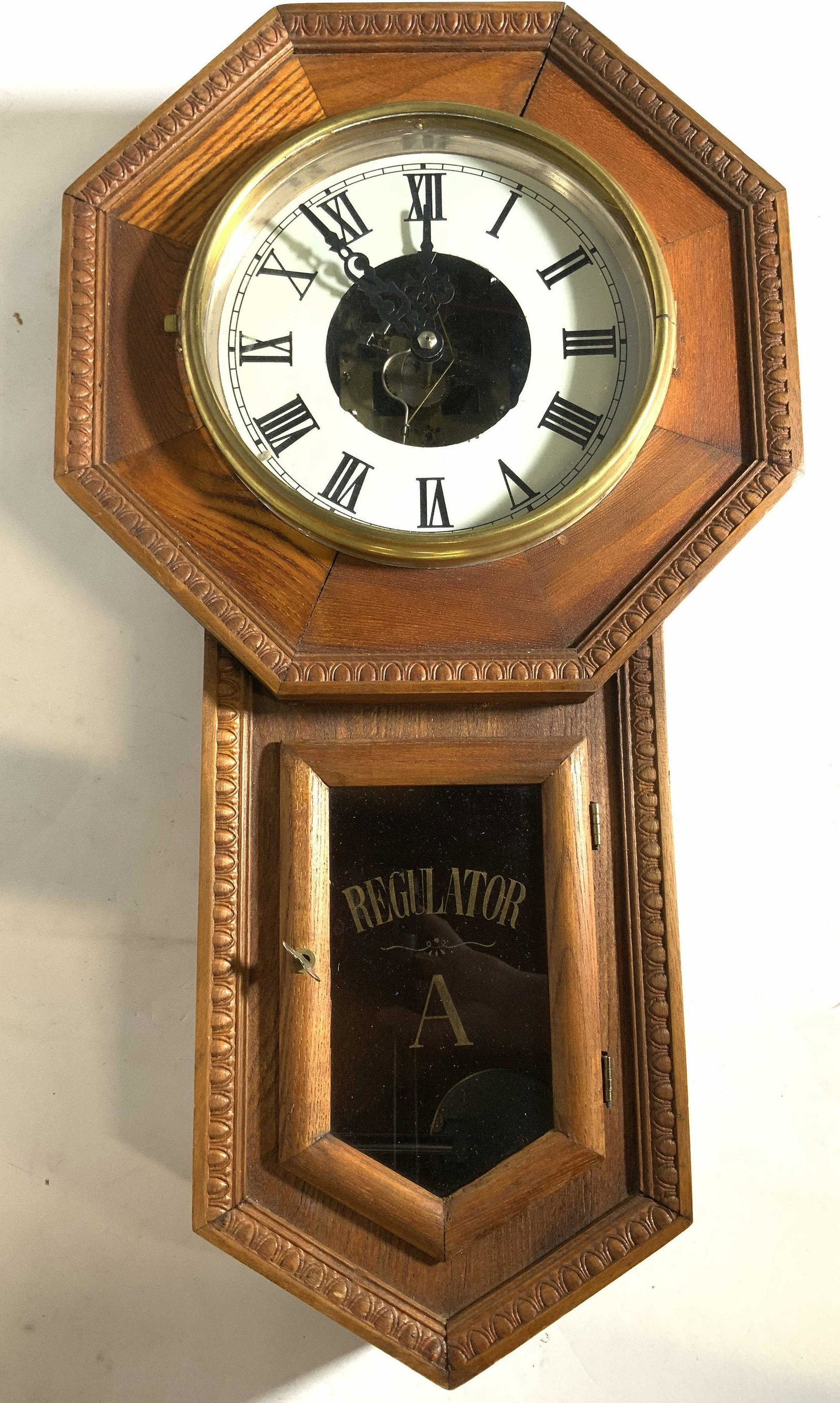 REGULATOR Antique Wooden Wall Clock: Clock is marked REGULATOR on lower window. Top half of clock has octagonal shape, circular glass window revealing a white toned clock face with black toned Roman numerals and hands. Lower window has s