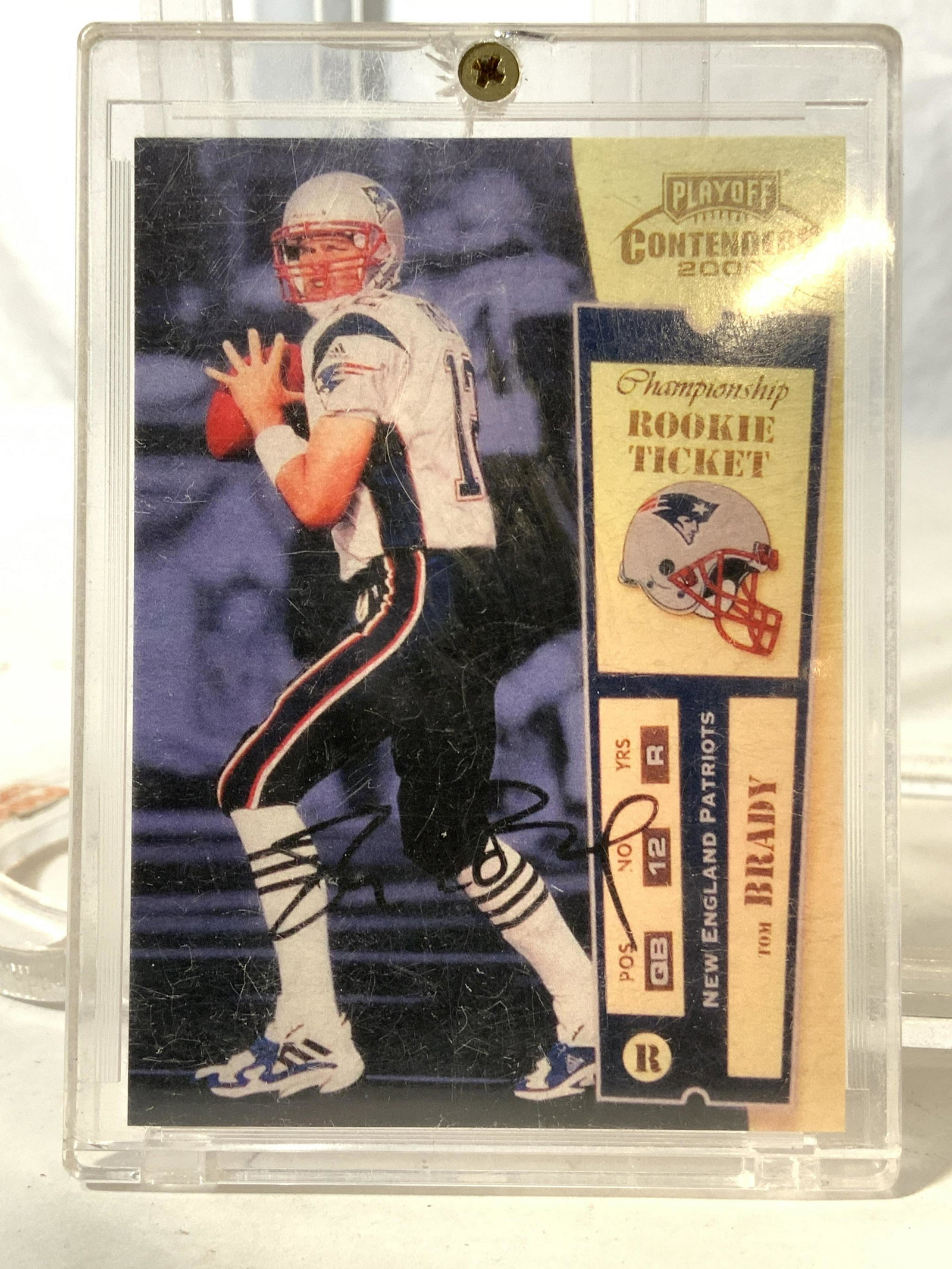 TOM BRADY Playoff Contenders Rookie Card No 144: Backside of card has college statistics and short biography. Front side reads PLAYOFF CONTENDERS 2000 CHAMPIONSHIP ROOKIE TICKET. Piece has image of Tom Brady and image of signatures. Card is in case.