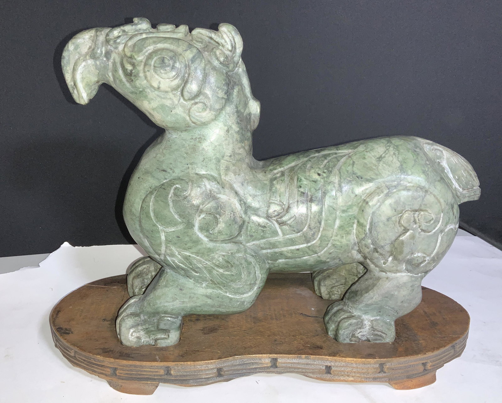 CHINESE JADE CARVED SCULPTURE of Mythical Creature: Asian Decor, stature on carved wooden stand with thunder cloud design. Stand is footed and has carved areas for a perfect fit of the statue. Crafted of a solid Piece of Jade. Possibly nephrite Jade. C