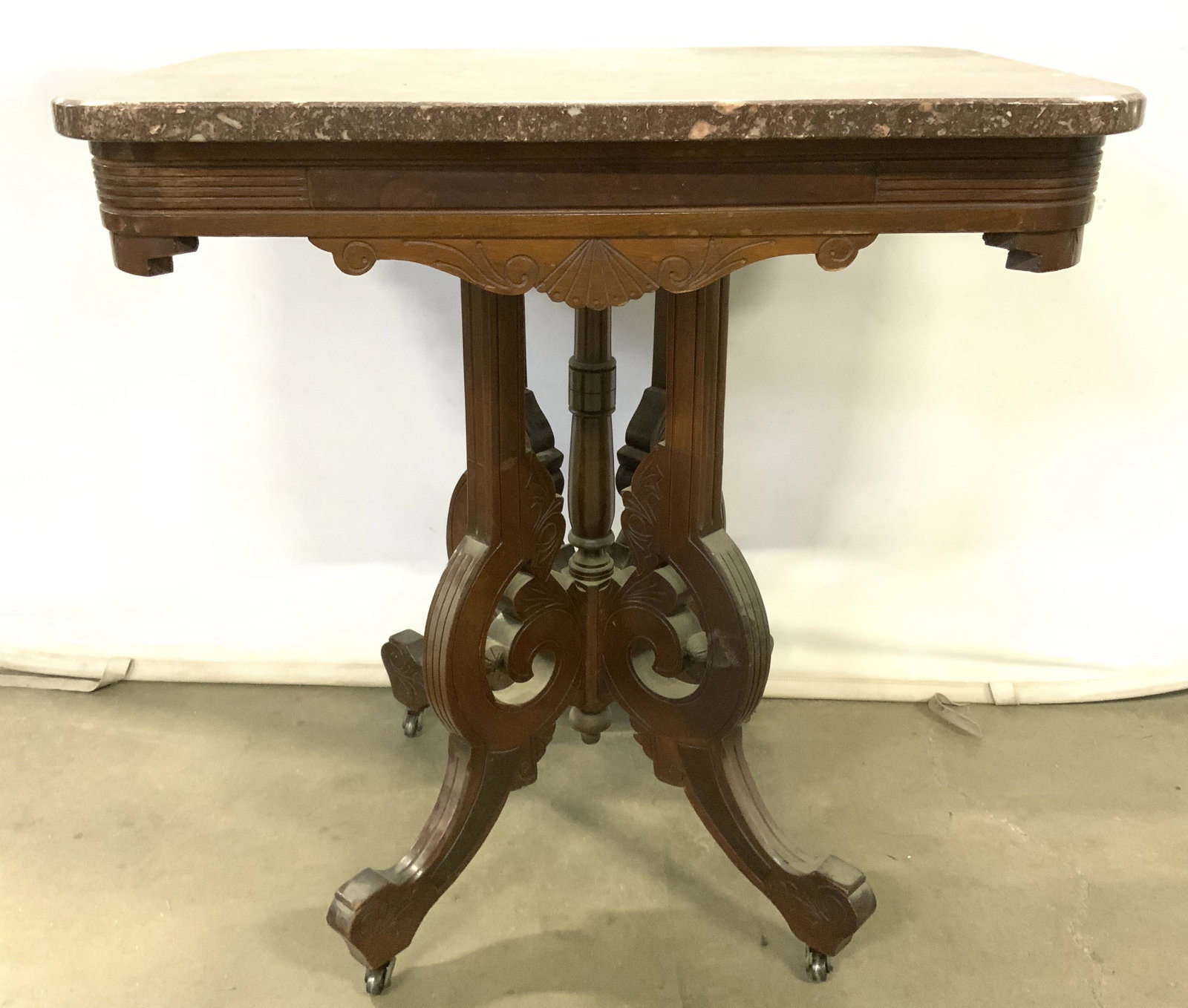 Antique Victorian East Lake Marble Top Table: Table has rounded rectangle shaped marble top. Table sits on 4 metal casters. Piece has 4 intricately carved wooden legs which meet at center. Table top support also has carved relief detail. Piece ha