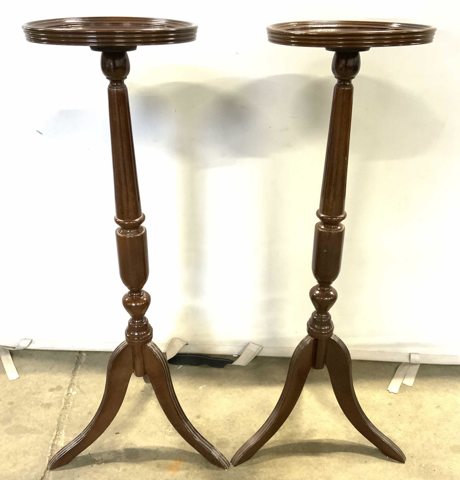 Pair BOMBAY COMPANY Carved Pedestal Tables: Undersides of pedestal tops have tags which reads THE BOMBAY COMPANY. Each are brown toned and wooden. Tabletops are round with raised edges. Each has tripod style feet. Each measures approx 35 inches