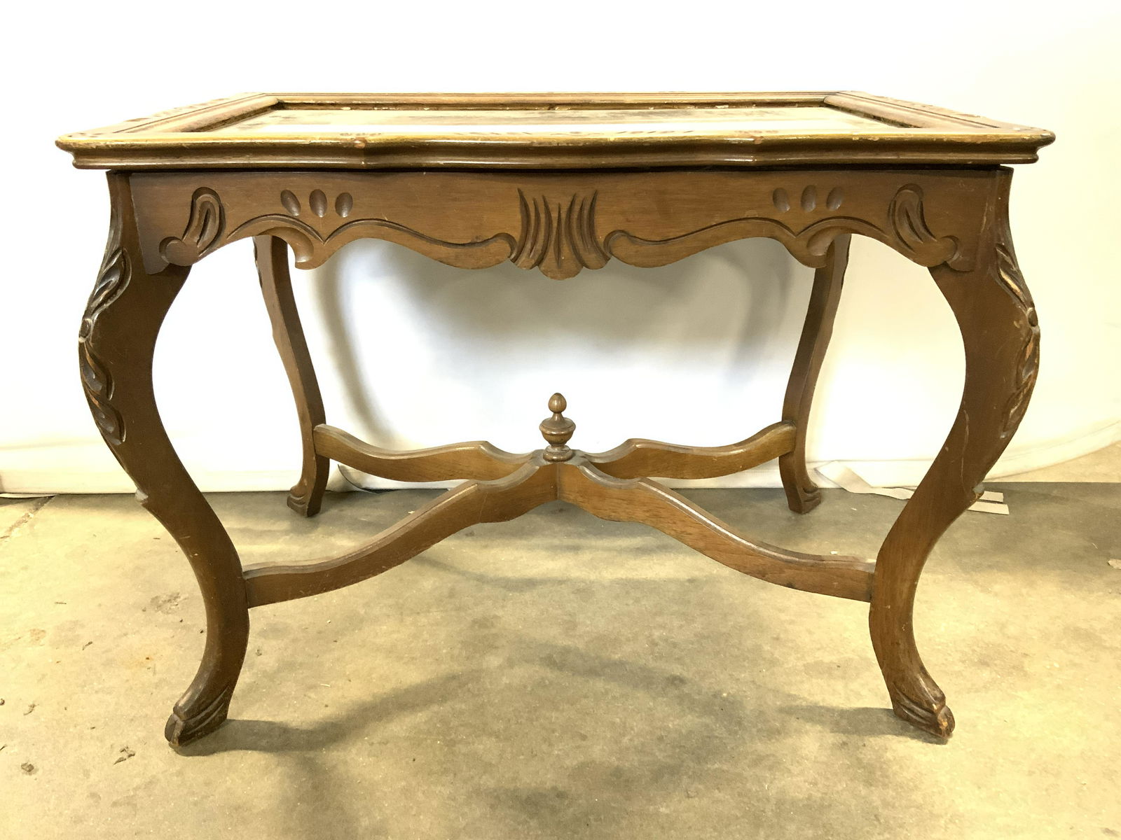 Vintage Wooden Glass Top Side Table: Table is vintage possibly antique. Piece has 4 carved wooden legs with s curve structure. Legs have carved wooden x stretcher in between with finial in center. Piece measures approx 27 inches long, 18