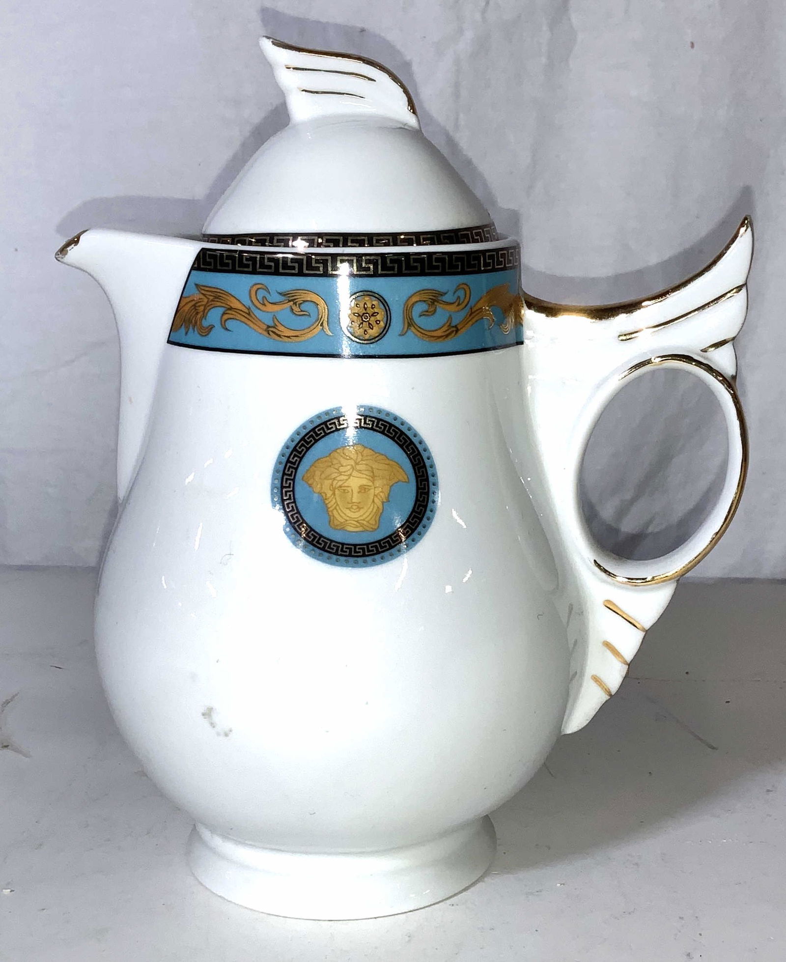 VERSACE Porcelain Teapot With MEDUSA LOGO: White porcelain teapot , gilt accents with gold and black Greek key pattern. One side displays the Versace Medusa head logo. Surface crack to lid and underside. Chip to inner diameter rim. Hallmarked