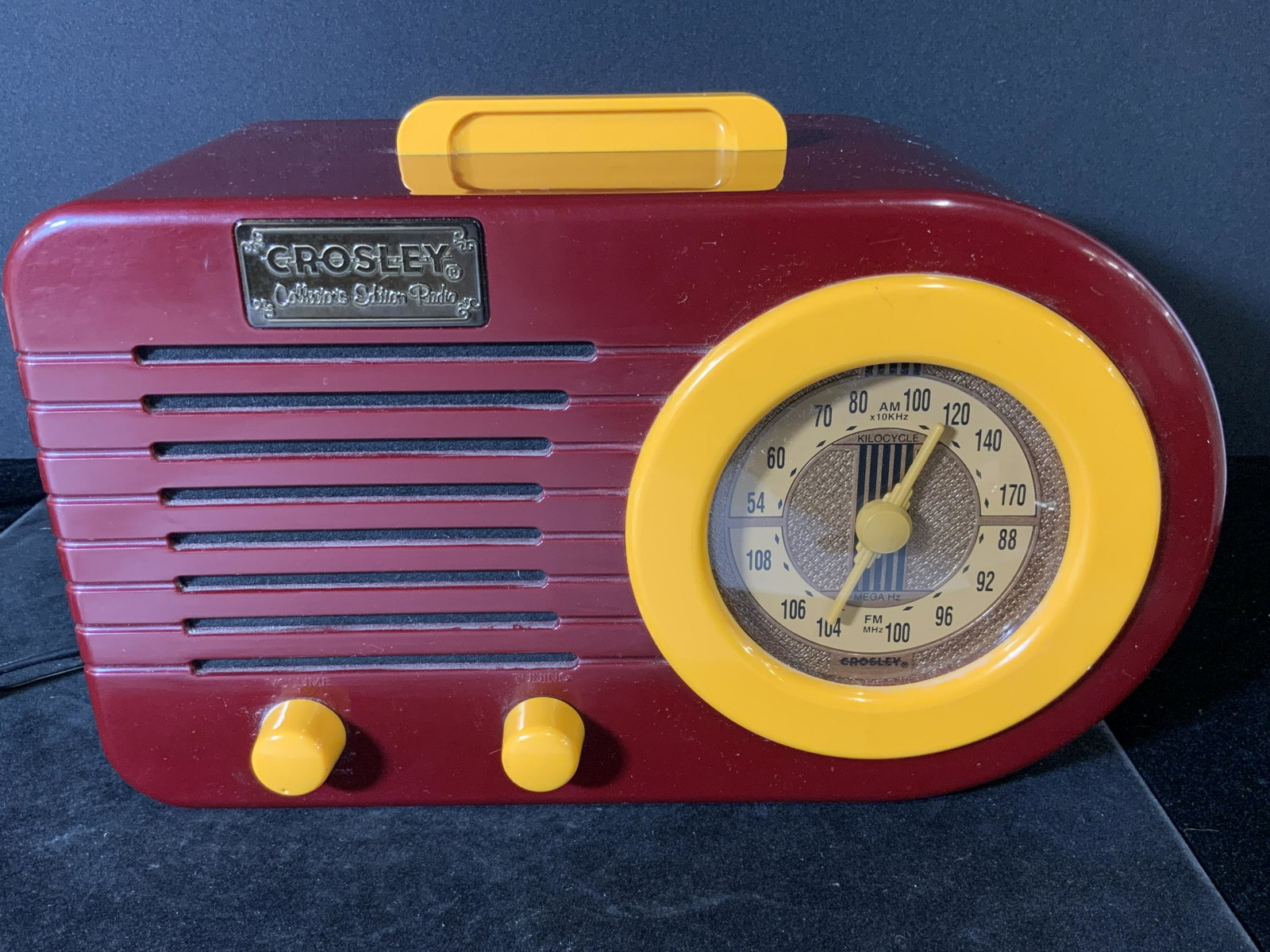 Vntg 1994 CROSLEY COLLECTORS EDITION RADIO, LE: Vintage C. 1994 collectible CROSLEY Model CR2 Collectors Edition Radio, bullet style radio. Maroon body with one rounded end and yellow hued handle, dials, and knobs. Buttons are turntable. Has an are