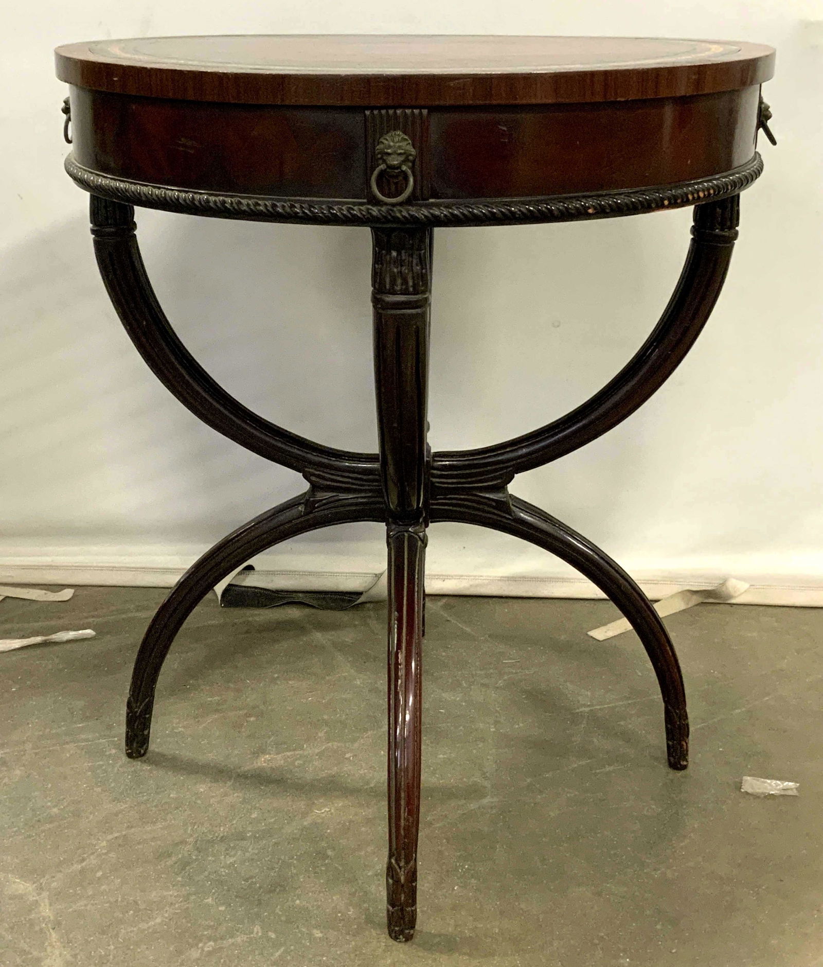 Antique Leather Top Round Wooden Side Table: Side table is vintage possibly antique. Piece has a red toned leather top with gold toned accent detail near edges. Piece measures approx 29 inches tall 25 inches wide. Side table has gold toned lion