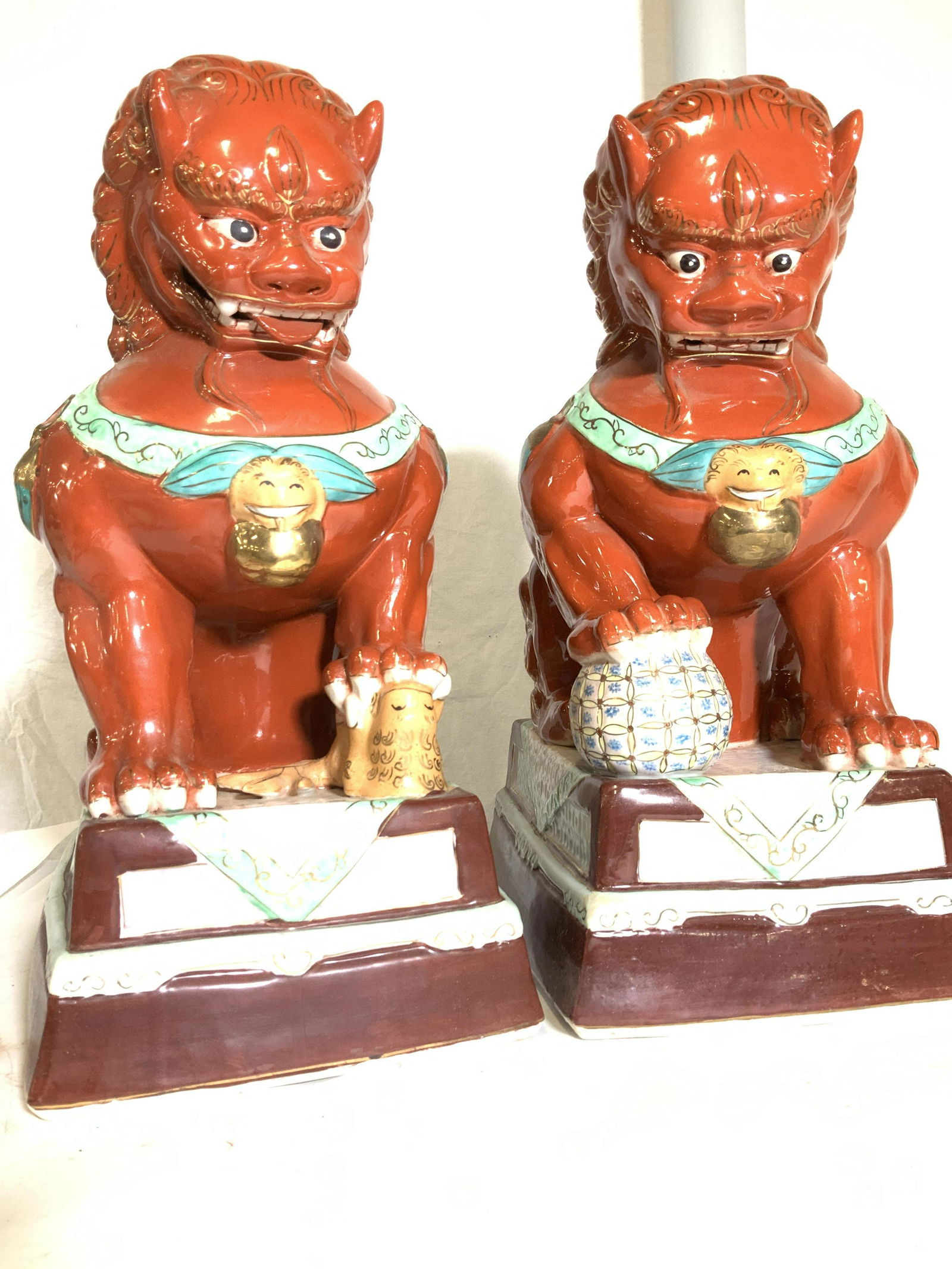 Pair Hand Painted Chinese Temple Dog Porcelain: Fierce temple guardian dog statues, one with paw on a ball, one with paw on a bird. All orange patina accented with aqua, gilt & Seafoam colors. All hand painted. Porcelain vent holes on verso. These