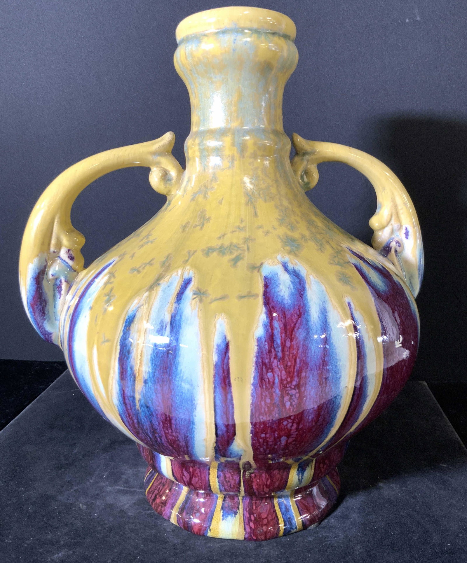 Handmade Artisan Oversized Ceramic Tabletop Vase: A handmade glazed ceramic tabletop vase with twin handles. Primarily yellow toned with maroon & blue hues accents colors. Thick walled ceramic. Weighty. Wear consistent with use, crazing, some wear to