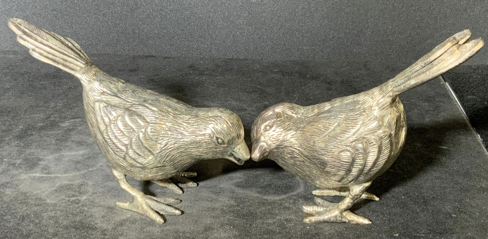 Pair Standing Silver Tone Metal Bird Figurals: Precisely etched silver tone metal bird figurals. The pieces stand alone. Birds are depicted in two different poses. Both have bowed heads and raised tail feathers. Some felt on the undersides of each