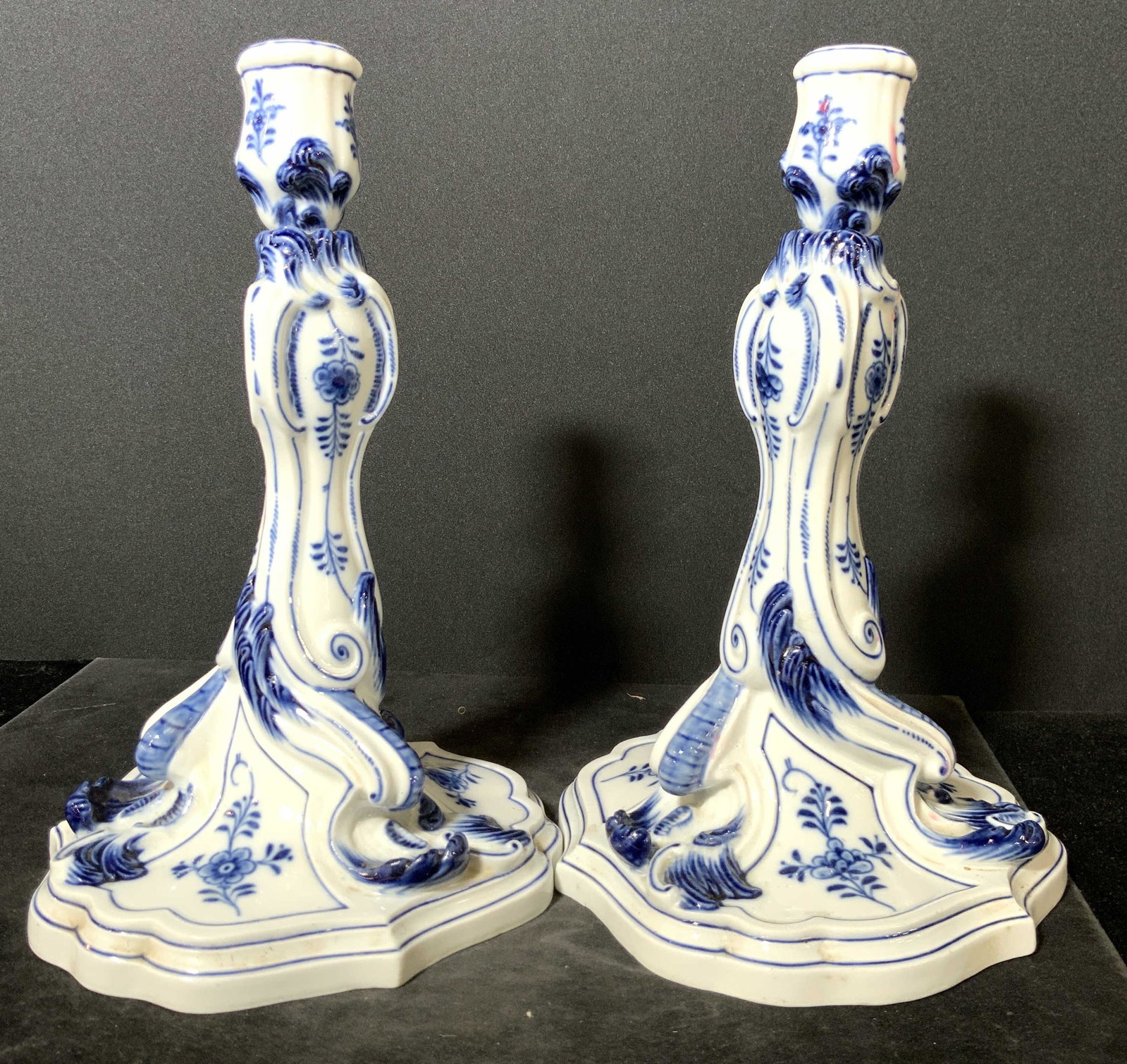 Pair Signed MEISSEN Porcelain Candlesticks: Two blue and white porcelain candlesticks. The pieces feature painted florals and nature motifs throughout. Embossed porcelain accents accent both pieces. The undersides are trademarked with the MEISS