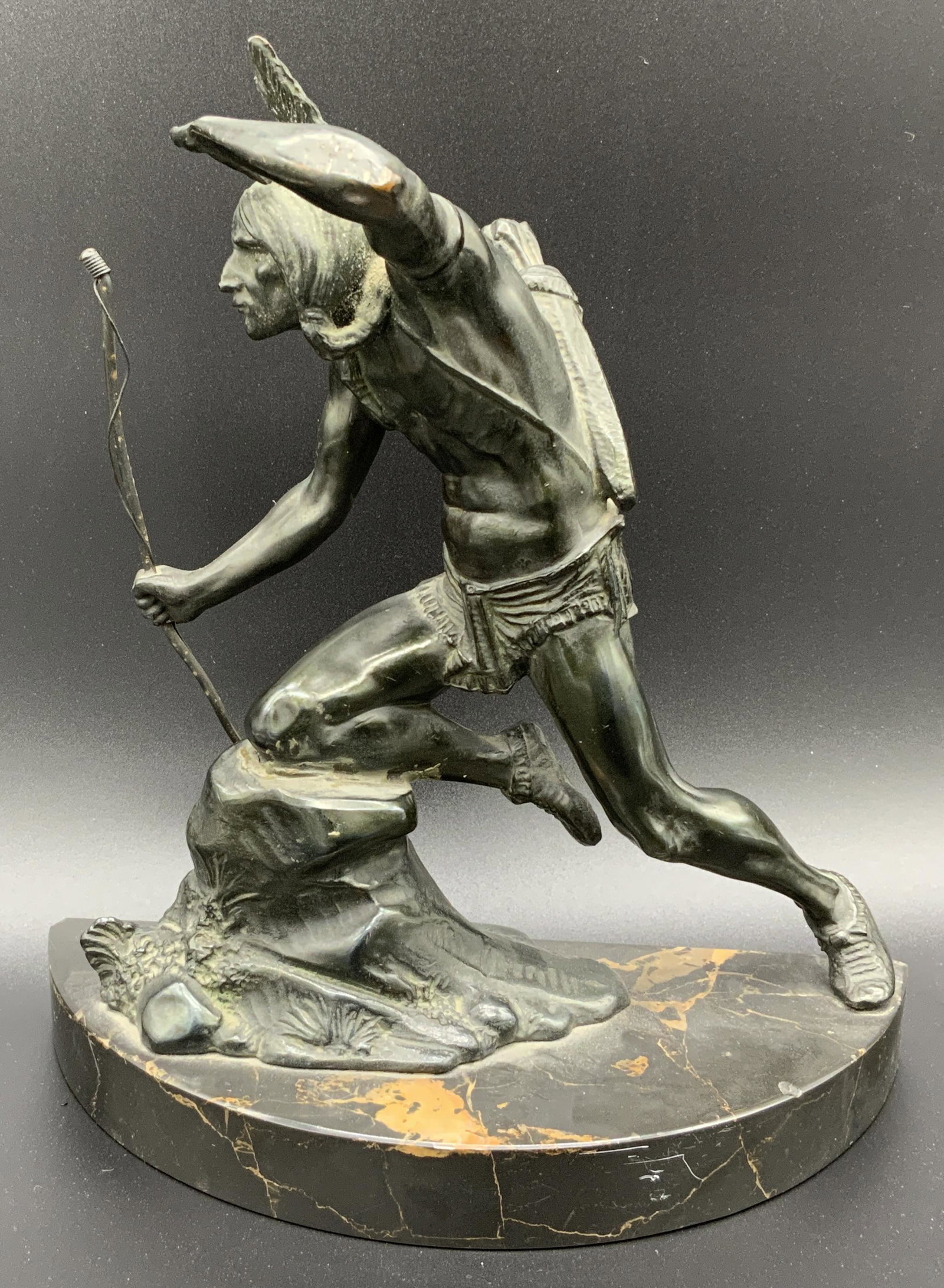 Hand Crafted Metal Statue of Native American: Hand crafted metal statue of Native American, stamp to backside of statue reads ‘769’, subject a Native American man holding a bow looking out into the distance, piece on a semi circle platform po