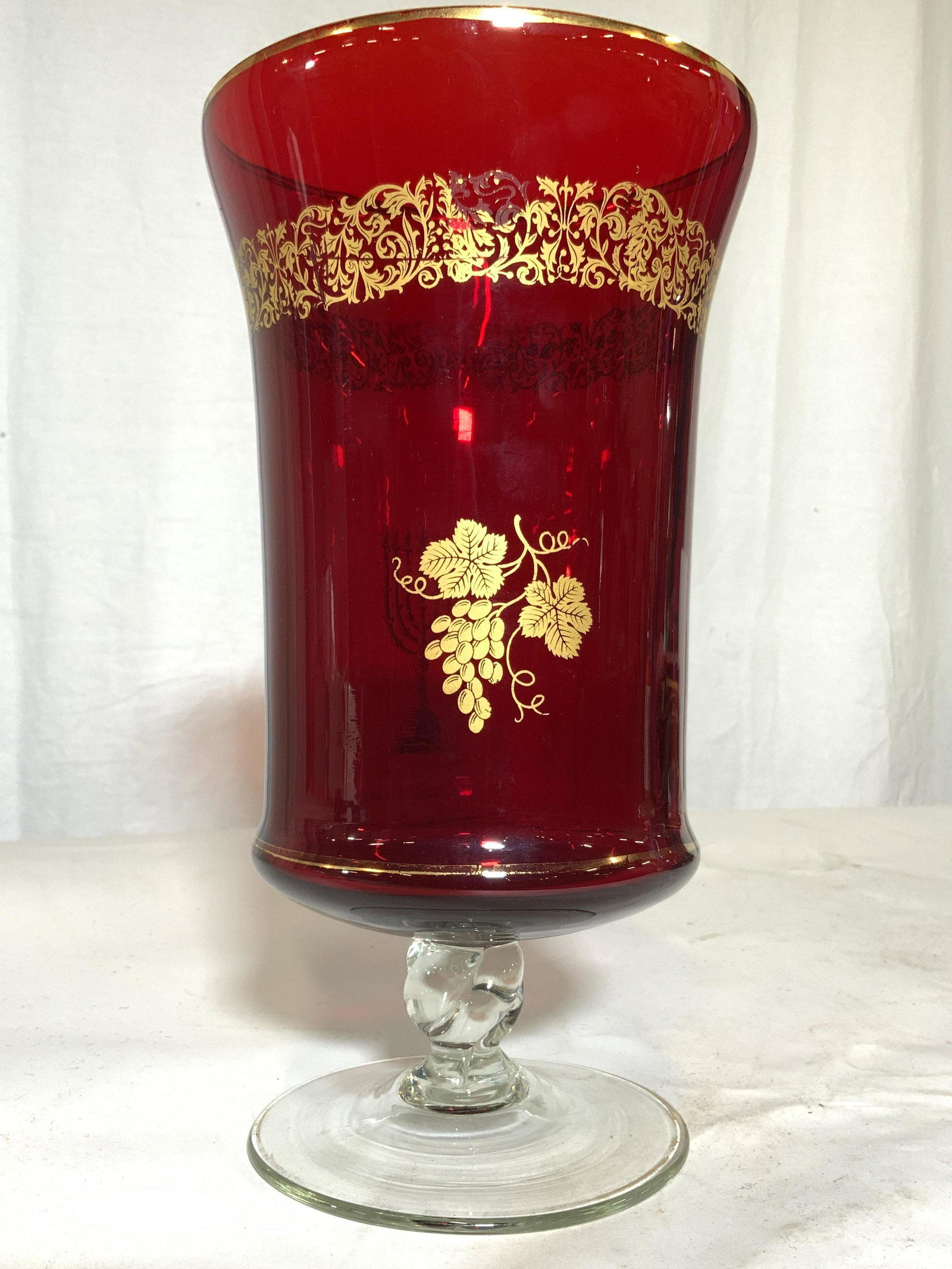 MURANO Glass Pedestaled Art Glass Vessel: Vessel appears to be MURANO glass. Piece is cranberry with gold toned ornate vine, leaf, grape & candelabra detail. Piece measures approx 10 inches tall 6 inches wide. MURANO Glass, Art Glass, Art Dec