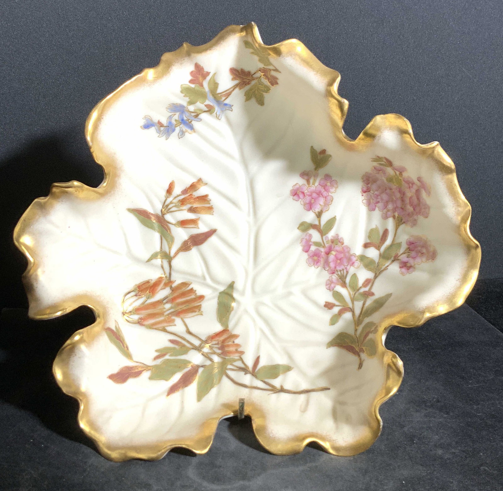 ROYAL WORCESTER Trademarked Porcelain Leaf Plate: A white porcelain leaf form plate with hand painted florals and gilt line work. The piece features ruffled edges, resembling the natural form of a leaf. Impressed porcelain accents within the center r