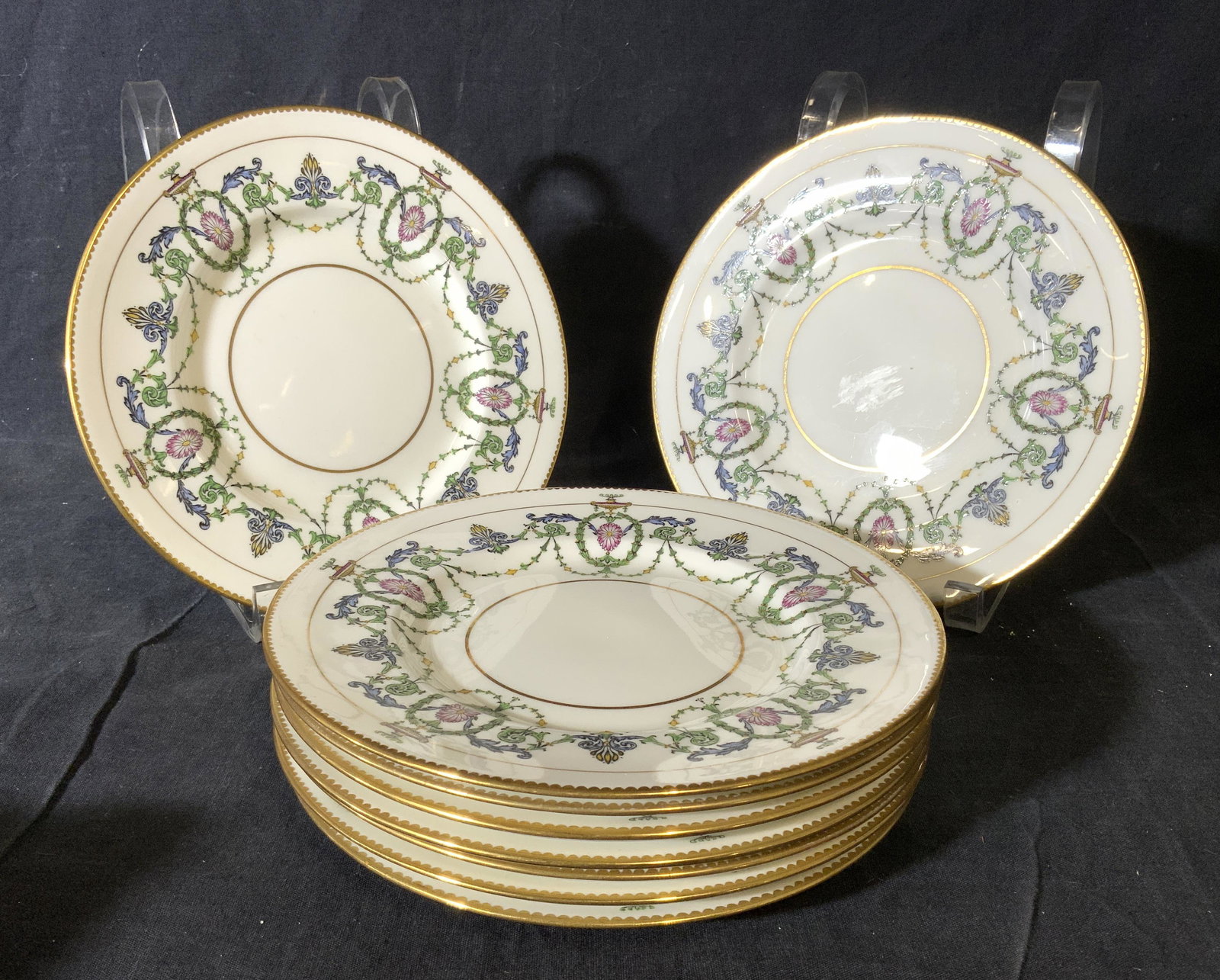9 MINTONS BURLEY & CO Chicago Porcelain Plates: Plates are marked MINTONS BURLEY & CO Chicago MADE IN ENGLAND on undersides. Lot includes a set of 9 porcelain plates. Each plate is white with multi toned floral & leaf garland style detail. Each mea