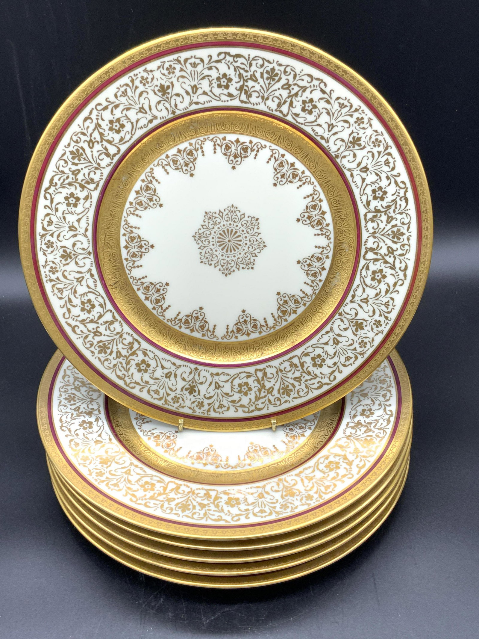 Set 6 DE LUXE DECORATING WORKS Plates, Czech: Set of six white porcelain dinner plates. Each plate features ornate heavy gilt accents and maroon banding. Some of the gilt accents are raised. The undersides are stamped CHATEAU CHINA, DE LUXE DECOR