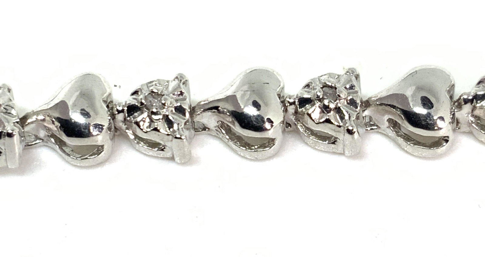 .15CT Diamond & Heart Link Tennis Bracelet W/ Box: A .15CT diamond tennis bracelet. The metal appears to be platinum. Every other polished metal bracelet link is accented with a diamond. The links in between a heart shaped. Piece secures with a box cl