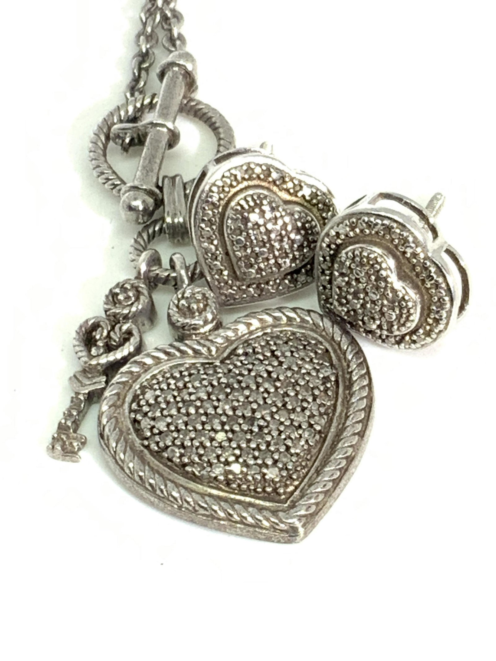 Set 2 DM STERLING SILVER Heart Necklace & Earrings: A set featuring a pair of heart form earrings and a necklace adorned with a heart charm. Both pieces are marked 925. Earrings are also marked DM. The necklace secures with a claw clasp closure, the ne