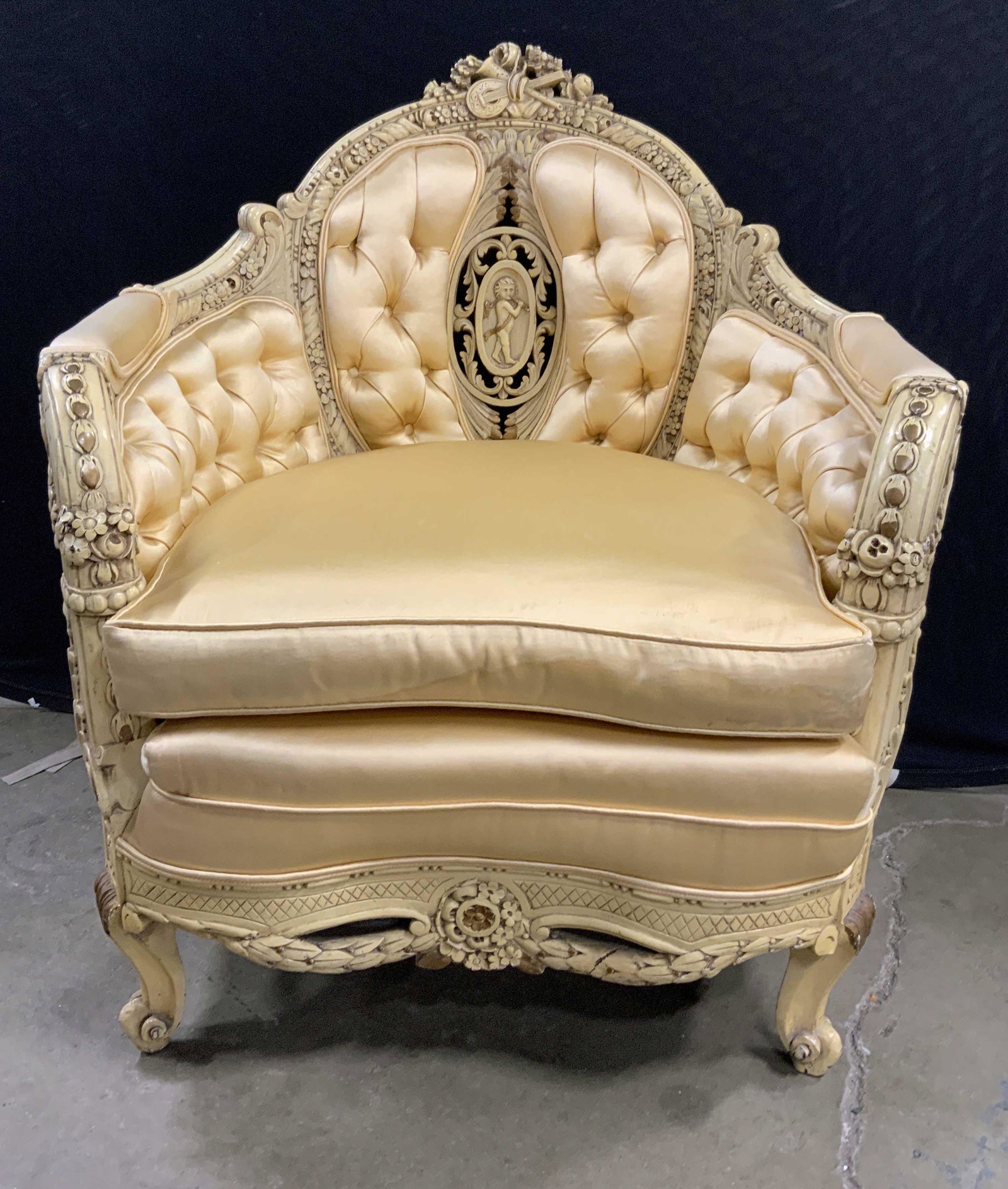Intricately Carved Upholstered French Armchair: Vintage, possibly antique, French provincial armchair. Wood creamer is hand painted and hand carved, decorated with intricate depictions of flowers and instruments. Upholstery and frame are cream tone
