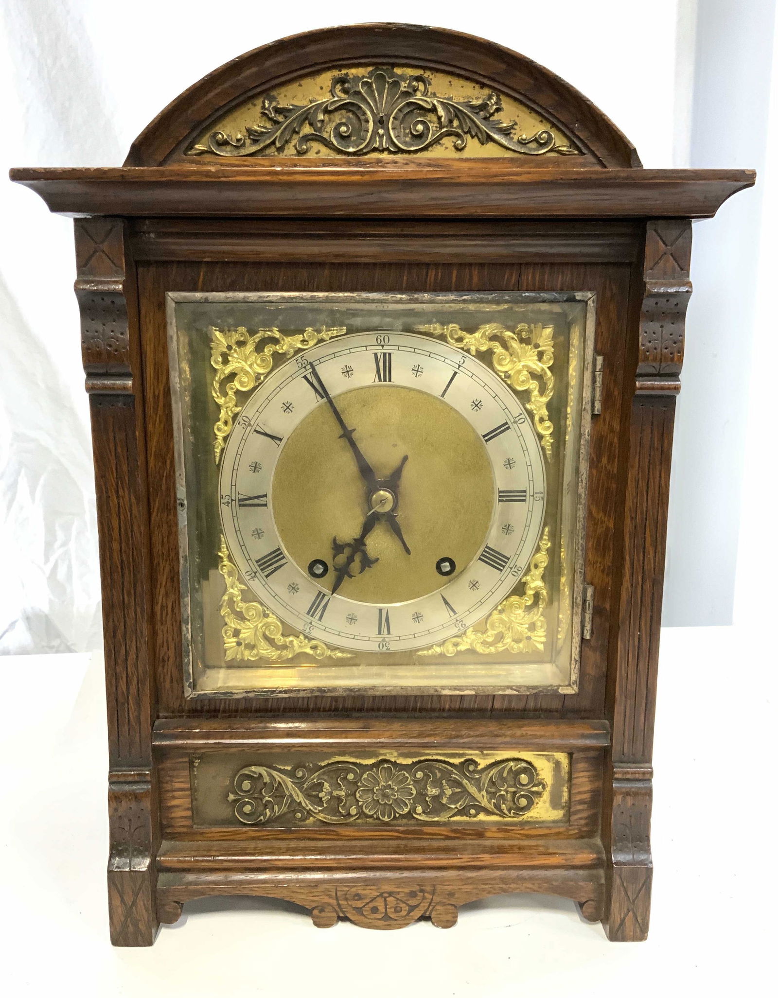 Vintage Wooden Mantle Clock: Vintage, possibly antique, wooden mantle clock. Clock face is metal, decorated by gilded metal, behind a hinged glass door. Decorative brass detailing located below and above clock face. A door on clo