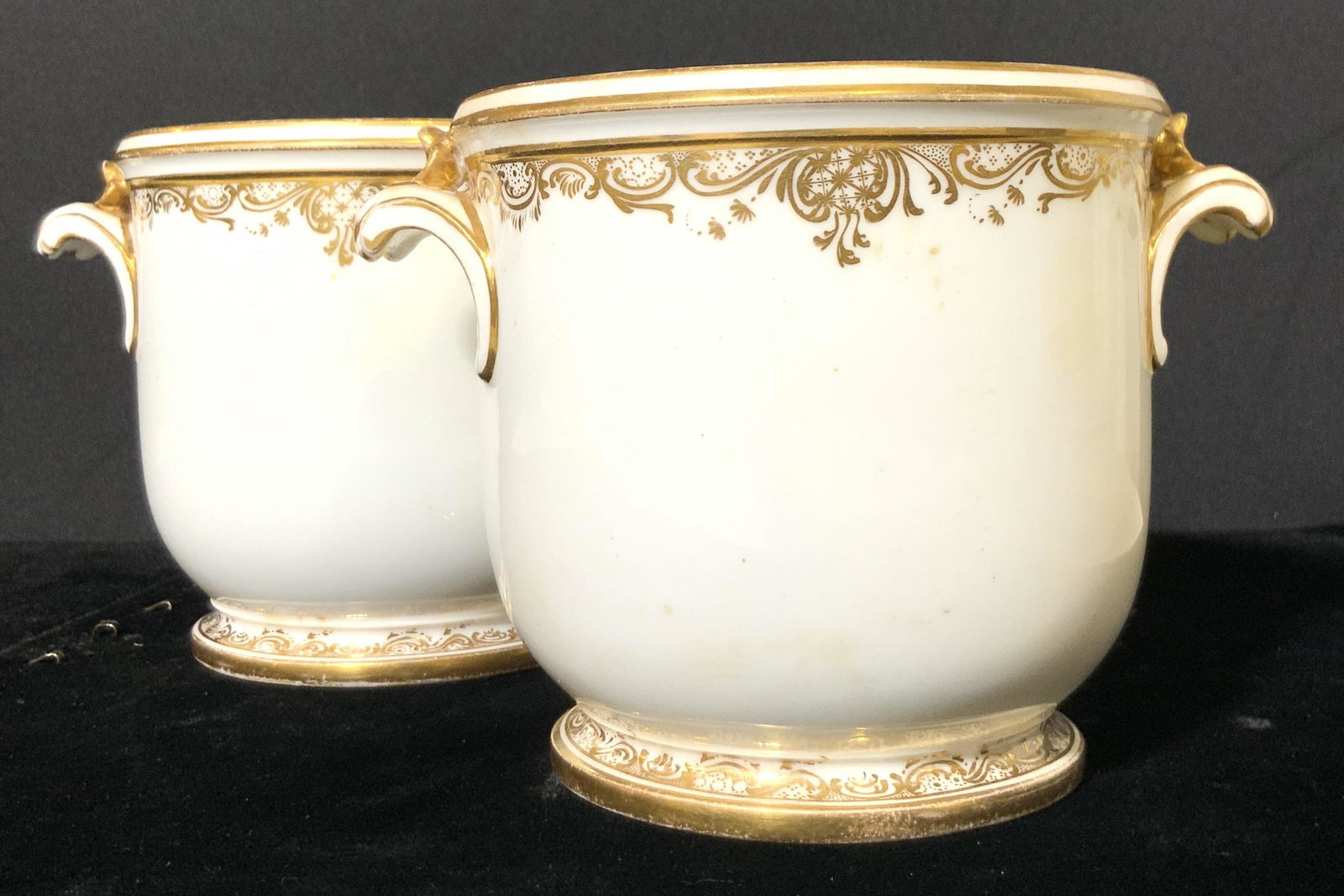 Pair White Porcelain Gilt Rimmed Cachepots: Two matching white porcelain cachepots with gilt accents along the rims and bases. Each cachepot has twin handles. Mild wear to gilt paint. Approx. 4H x 5.5W in. Porcelain cachepot, porcelain planter,