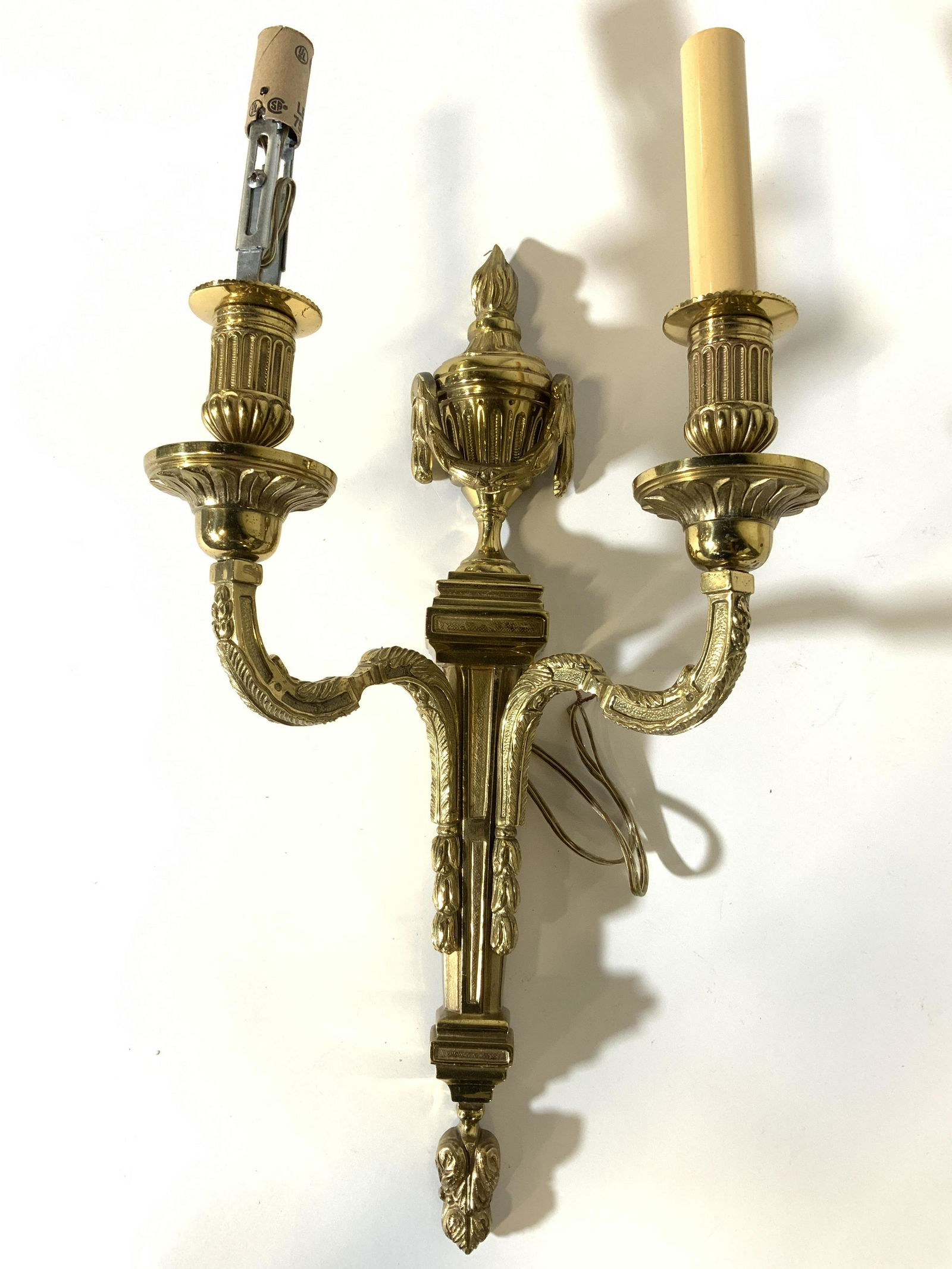 Vintage Gold Toned Brass 2 Arm Wall Sconce: Wall sconce is gold toned & brass. Piece has intricate ornate detail. Arms have s curve shape. Piece has 2 candlestick style bulb sockets. Wall sconce, brass wall sconce, vintage wall sconce, two arm