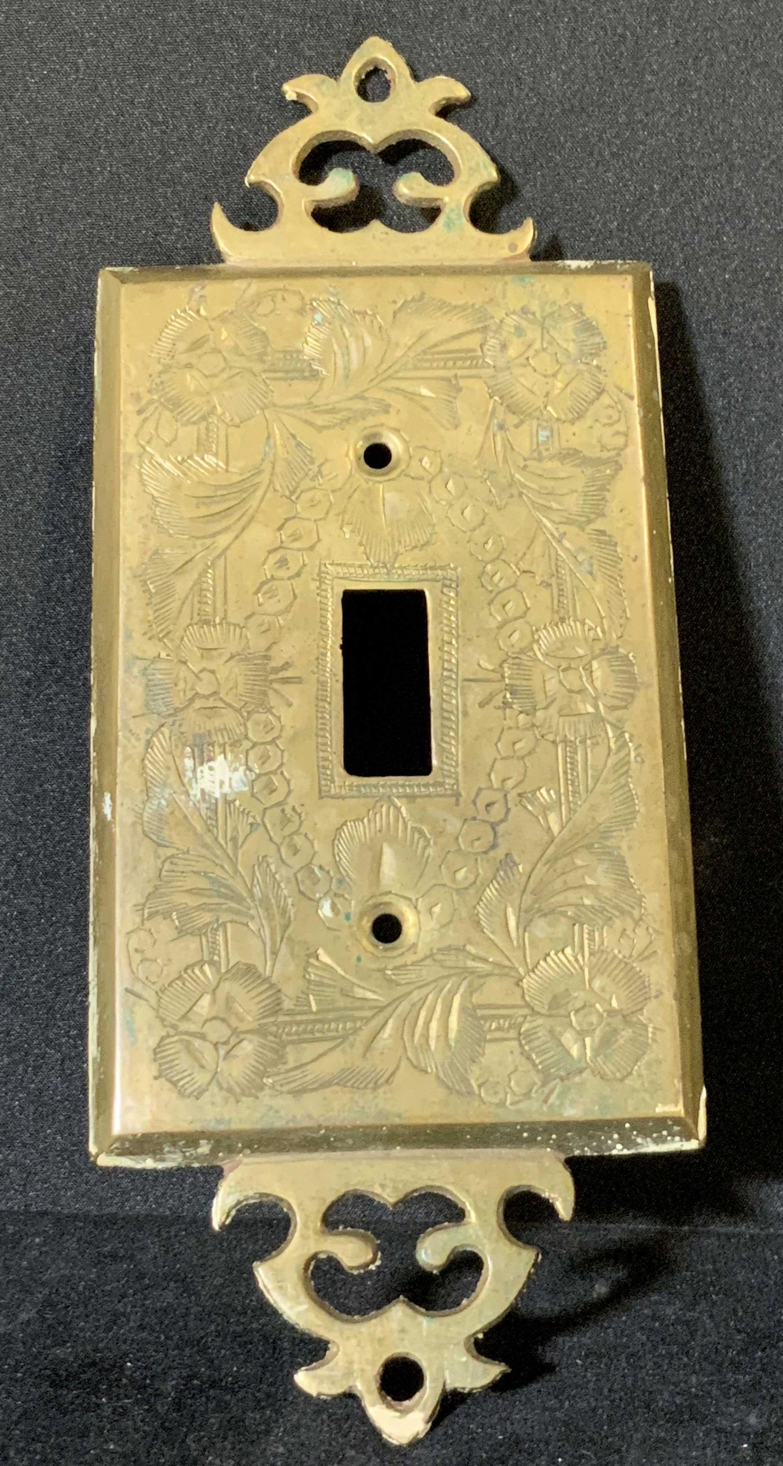 Metal Vintage Victorian Style Light Switch Cover: A metal, possibly brass, light switch cover. Piece is vintage and decorated with etched Victorian style designs throughout. Designs include florals. Underside reads: INDIA 2084. Approx. 7 x 3 in. Wear